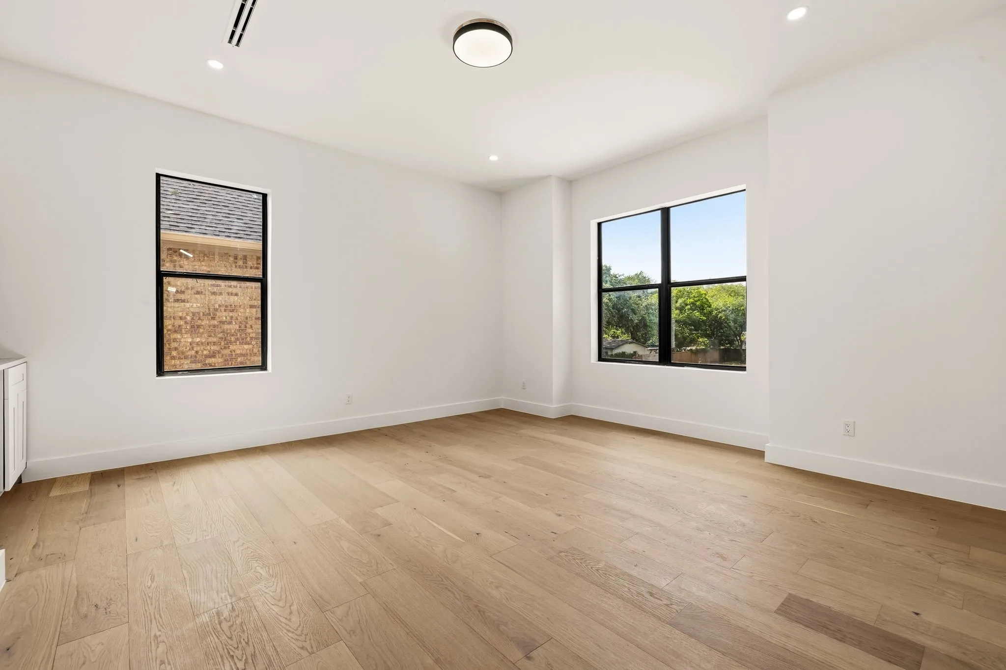 Spacious room featuring light wood-finish flooring, white walls, and recessed lighting