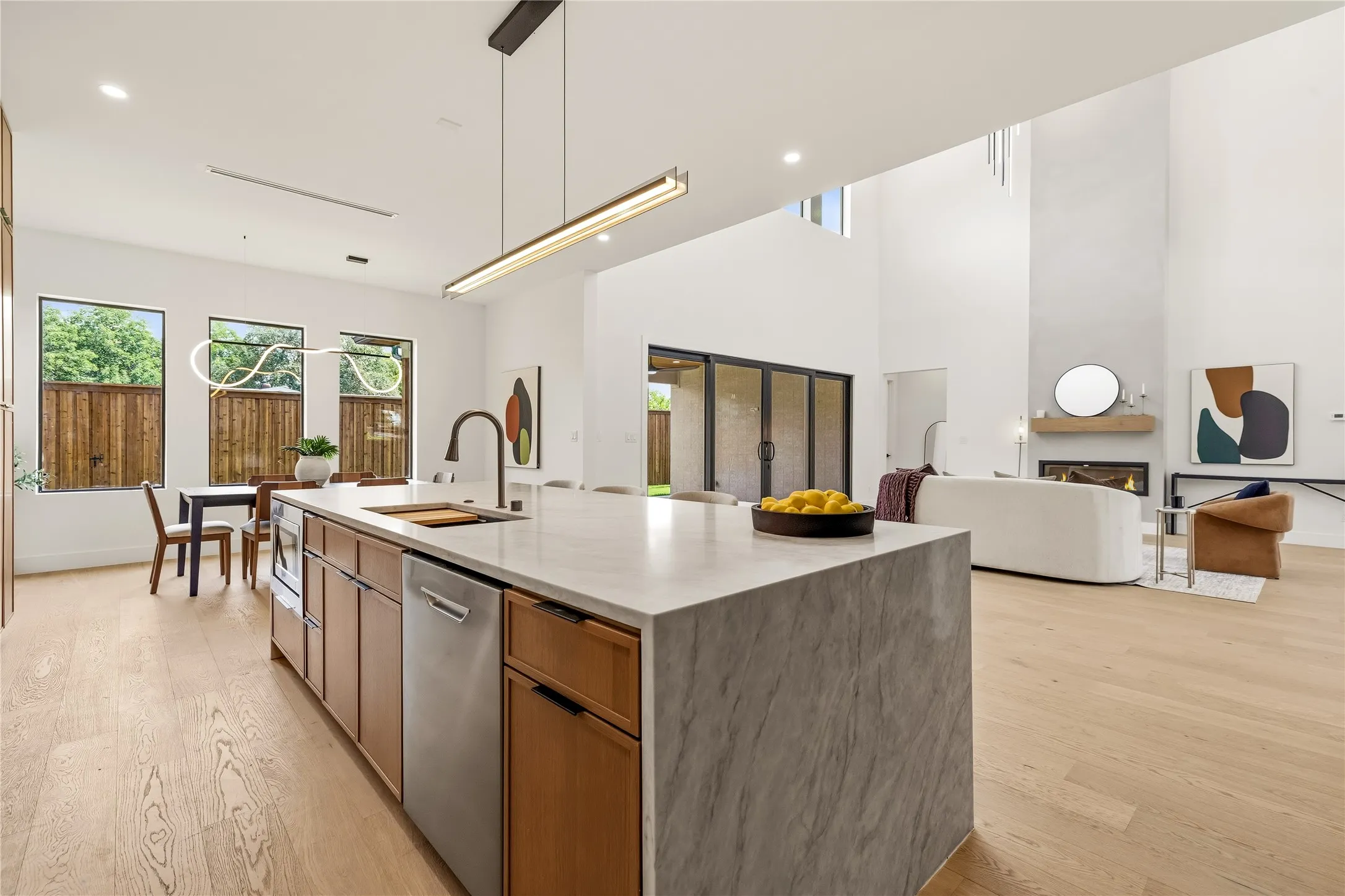Open-concept kitchen featuring an oversized island with waterfall stone countertop, integrated stainless steel appliances, and wood-finish cabinetry