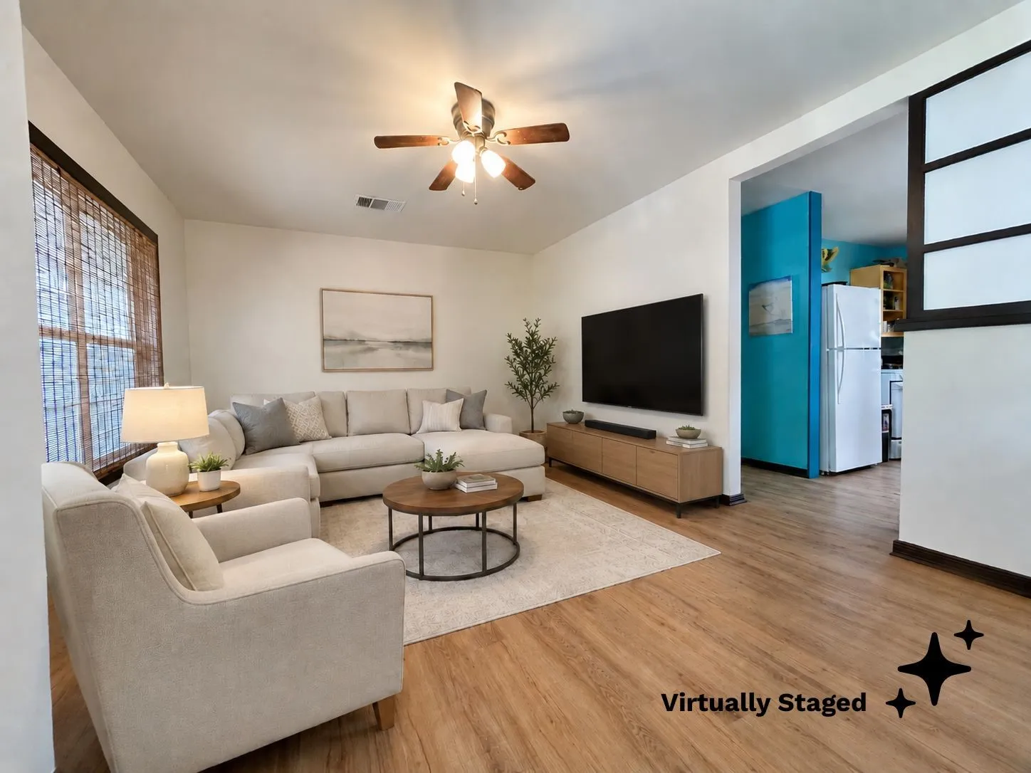 Living area featuring wood-finish flooring, a ceiling fan with integrated lighting, and a large window with bamboo blinds