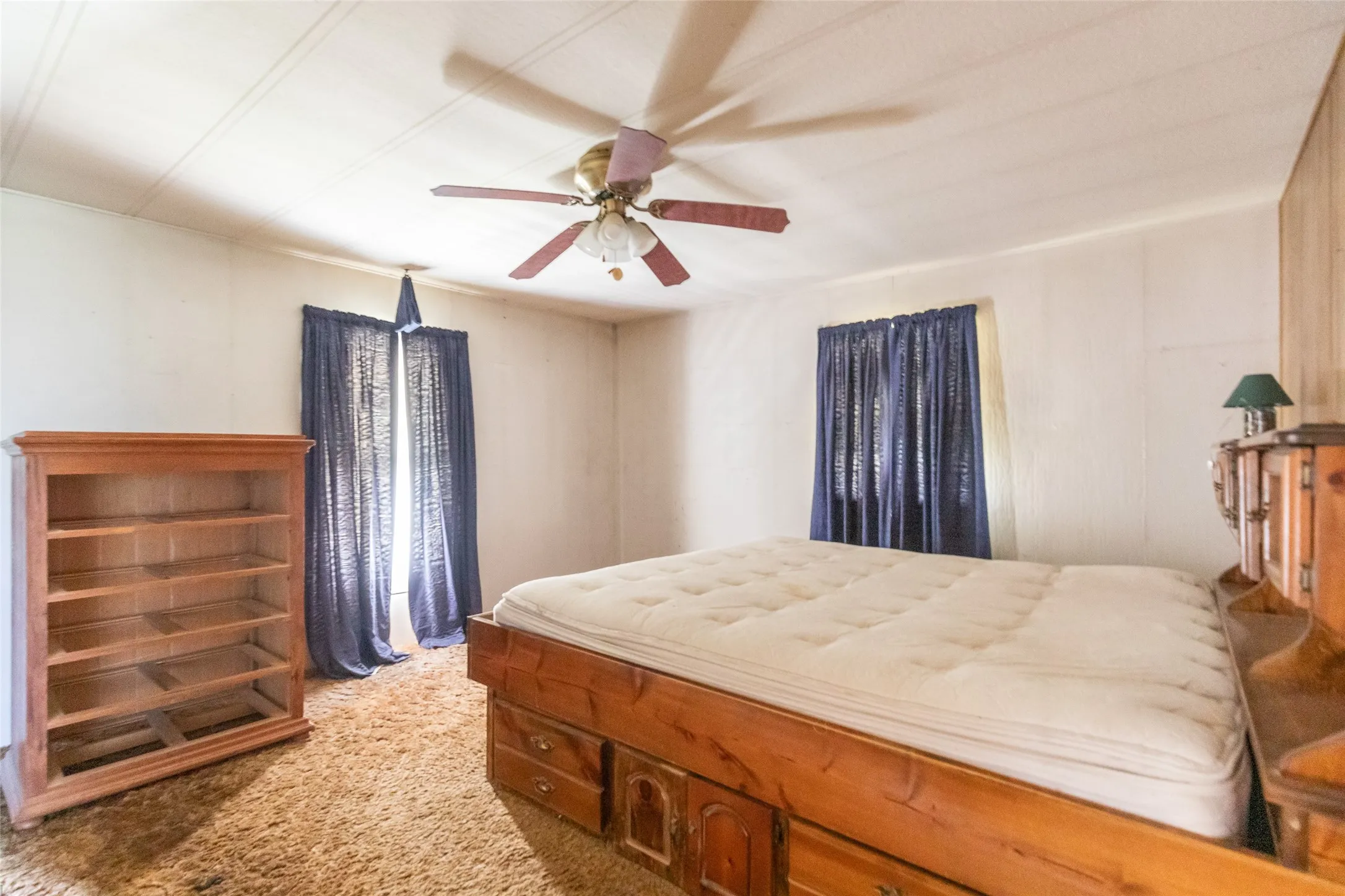 Interior room featuring a ceiling fan with integrated lighting, wood-finish wall paneling, and a window with dark curtains
