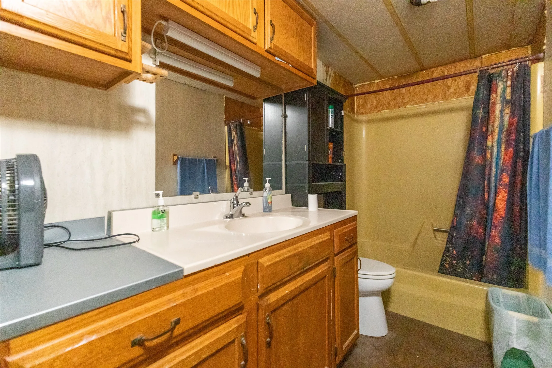 Bathroom featuring a wood-finish vanity with an integrated sink and countertop, wood-finish upper cabinetry, a mirror, and a bathtub with shower