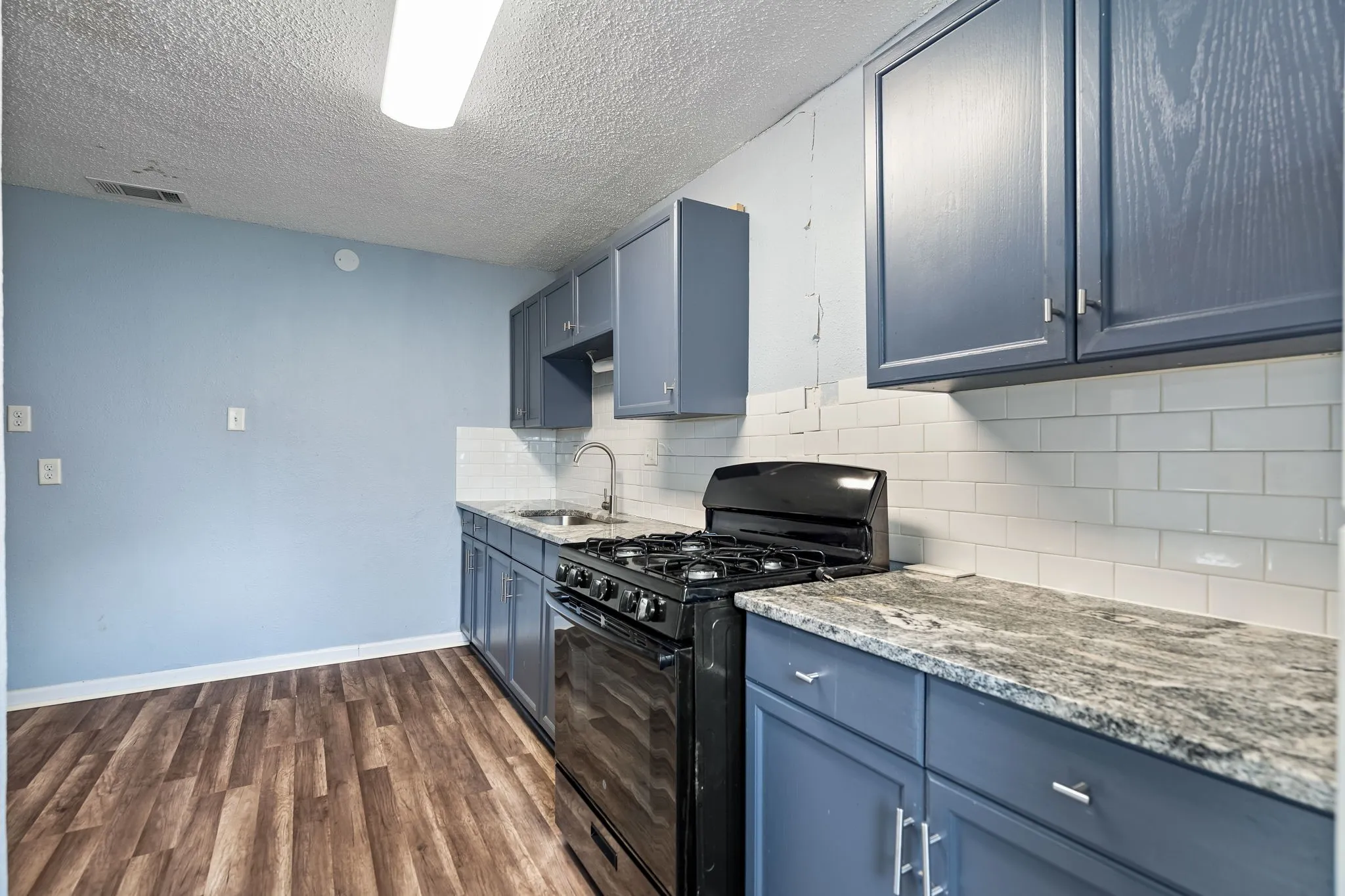 Kitchen with a textured ceiling, sink, blue cabinetry, black gas stove, and dark hardwood / wood-style floors