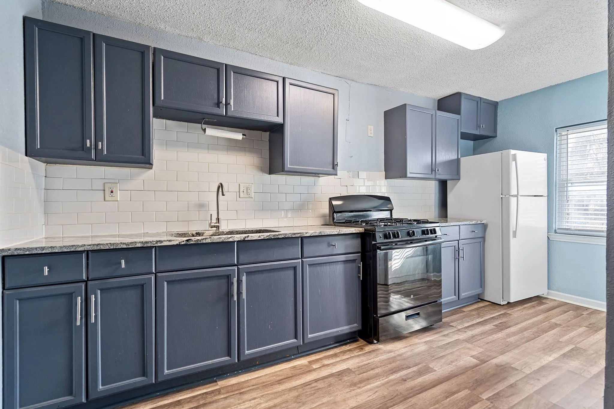 Kitchen featuring gas stove, sink, white refrigerator, backsplash, and a textured ceiling