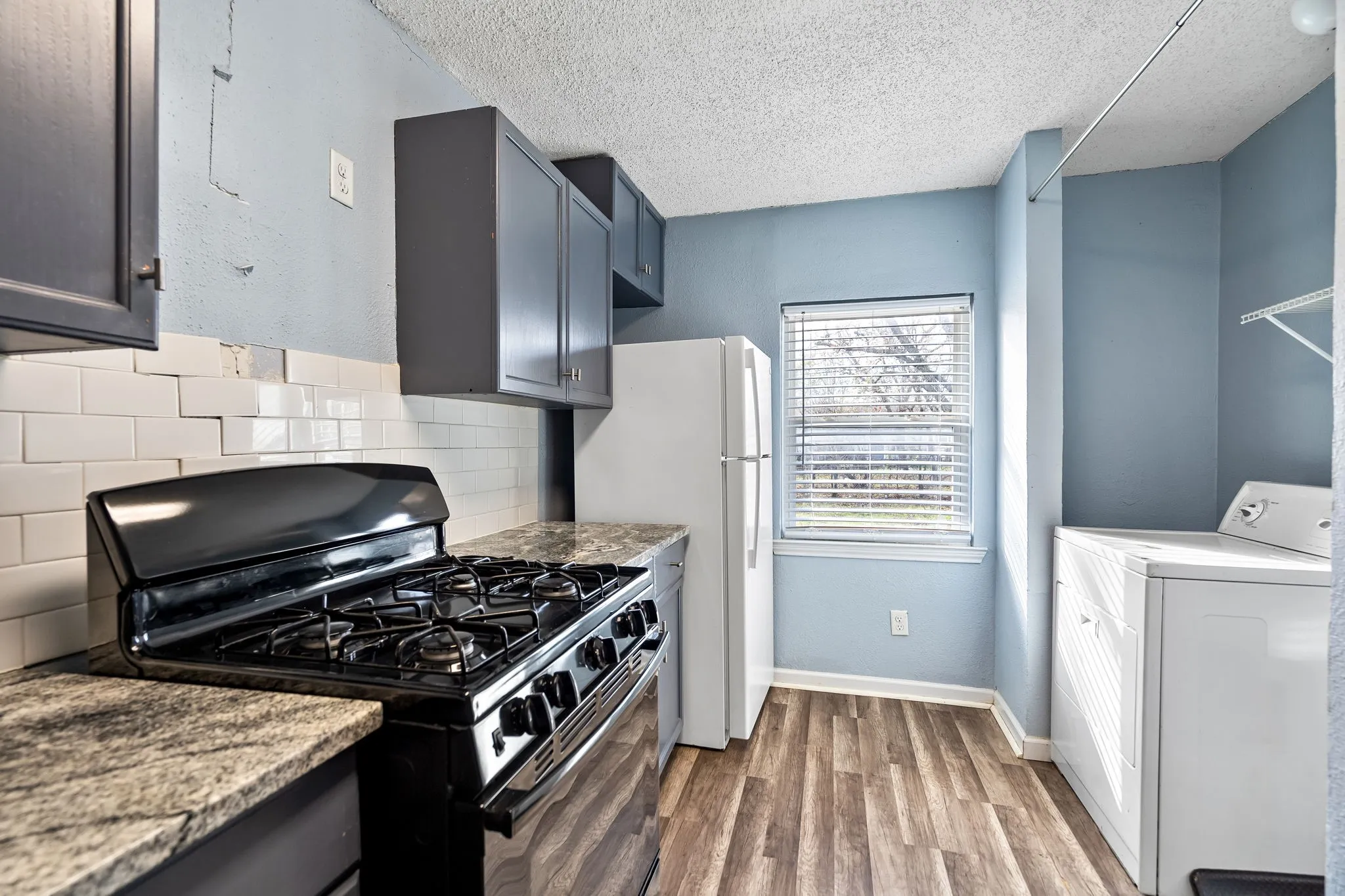 Kitchen featuring black gas range oven, tasteful backsplash, washer / clothes dryer, wood-type flooring, and a textured ceiling