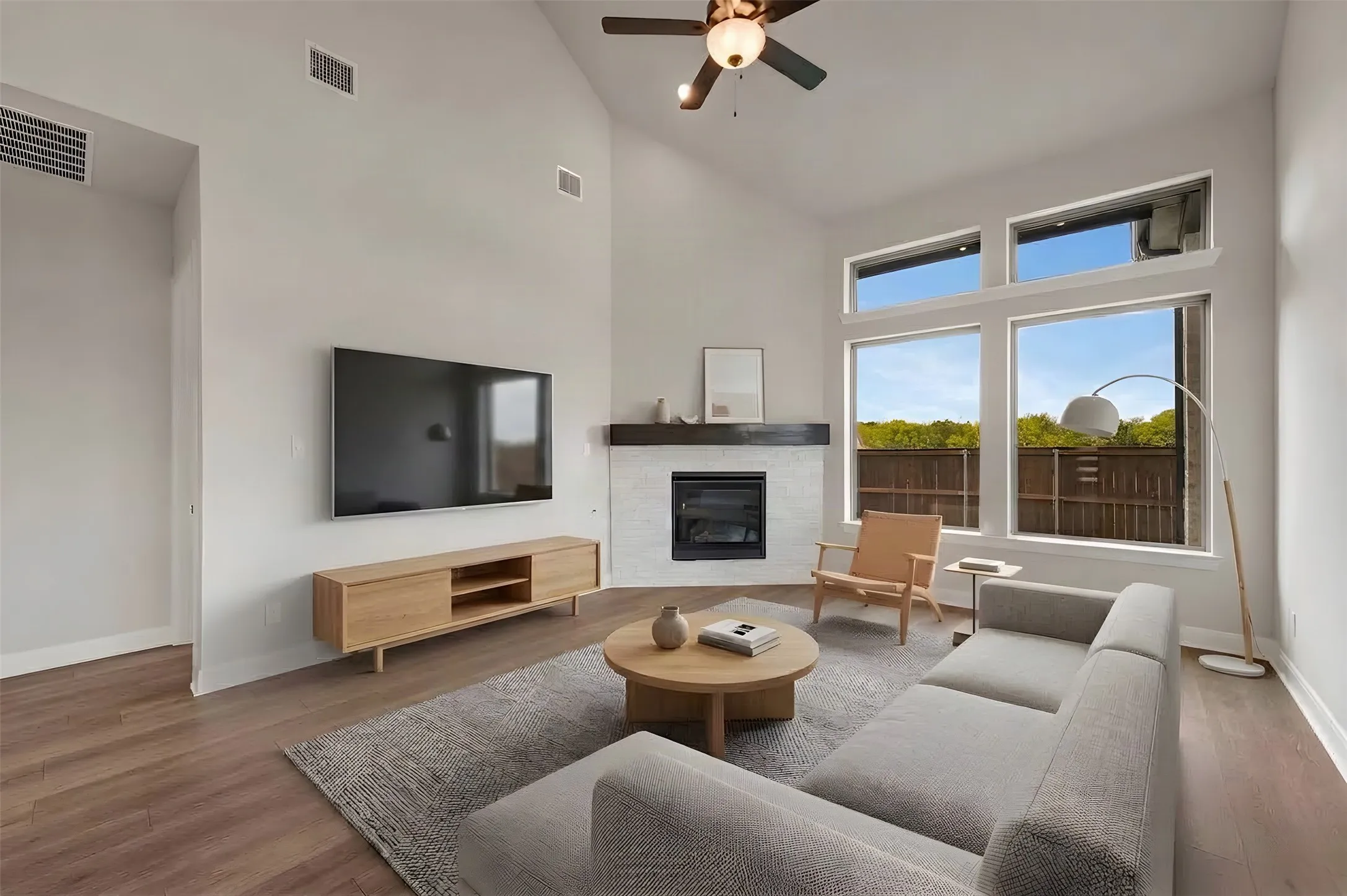 Vaulted ceiling with a ceiling fan, fireplace with a dark wood mantel, large windows, and wood-finish flooring