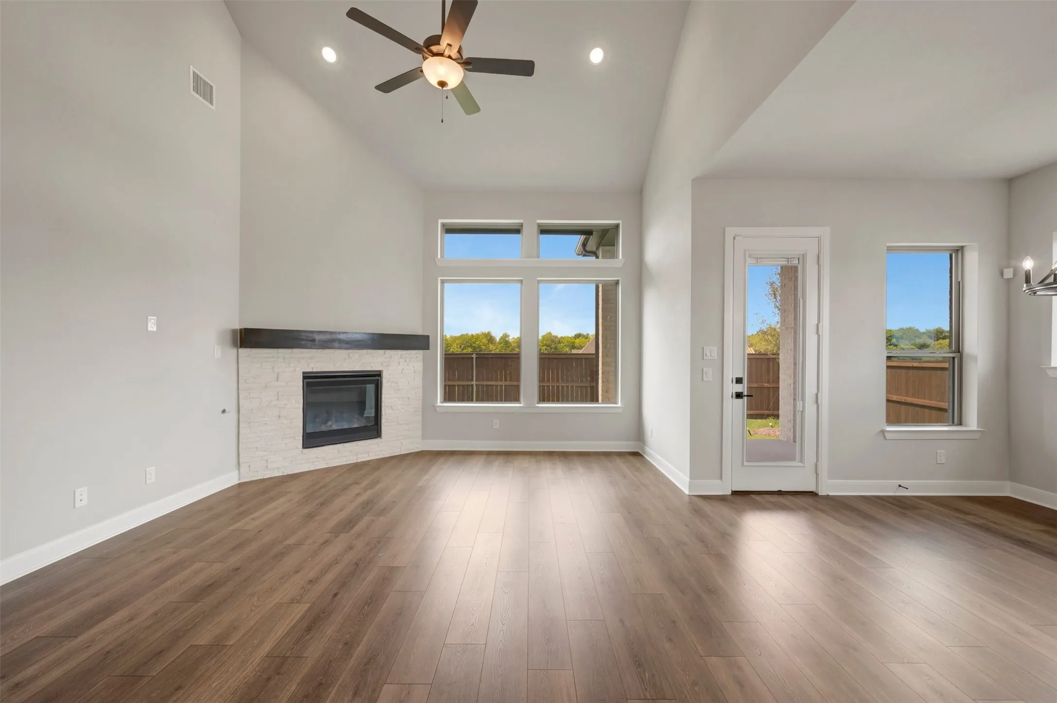 Vaulted ceiling with a ceiling fan, fireplace with a tile surround and wood mantel, wood-finish flooring, and multiple windows