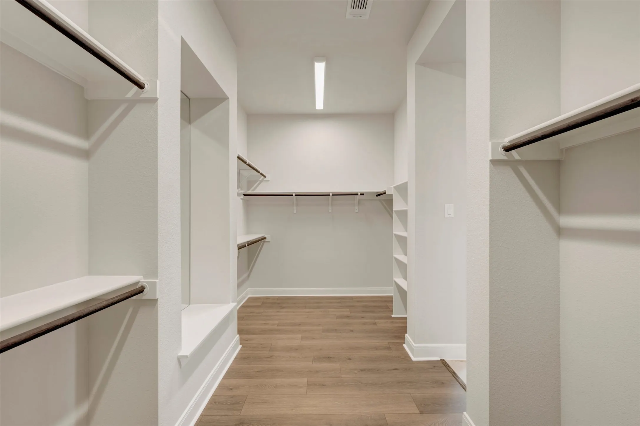 Expansive walk-in closet featuring wood-finish flooring, white walls, multiple shelving units, and hanging rods