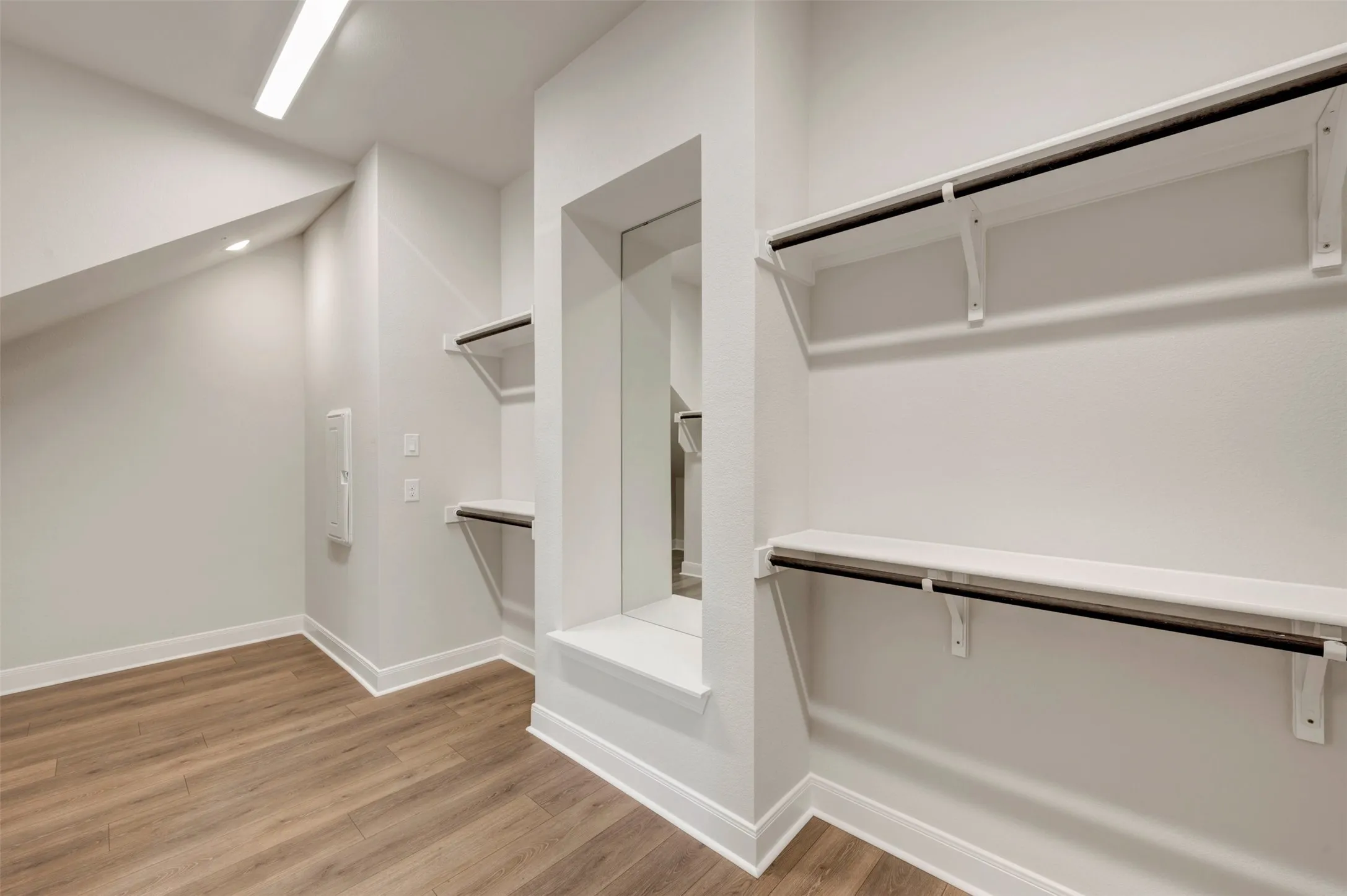 Expansive storage space featuring wood-finish flooring, built-in shelving, hanging rods, and an integrated mirror
