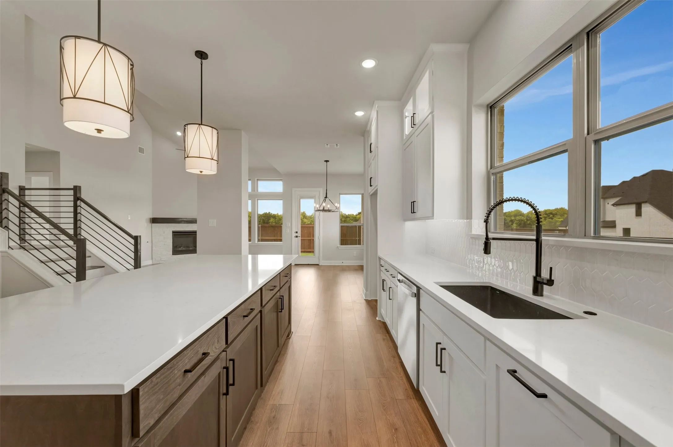 Spacious kitchen featuring an expansive center island with an integrated sink, crisp white cabinetry, light countertops, and wood-finish flooring