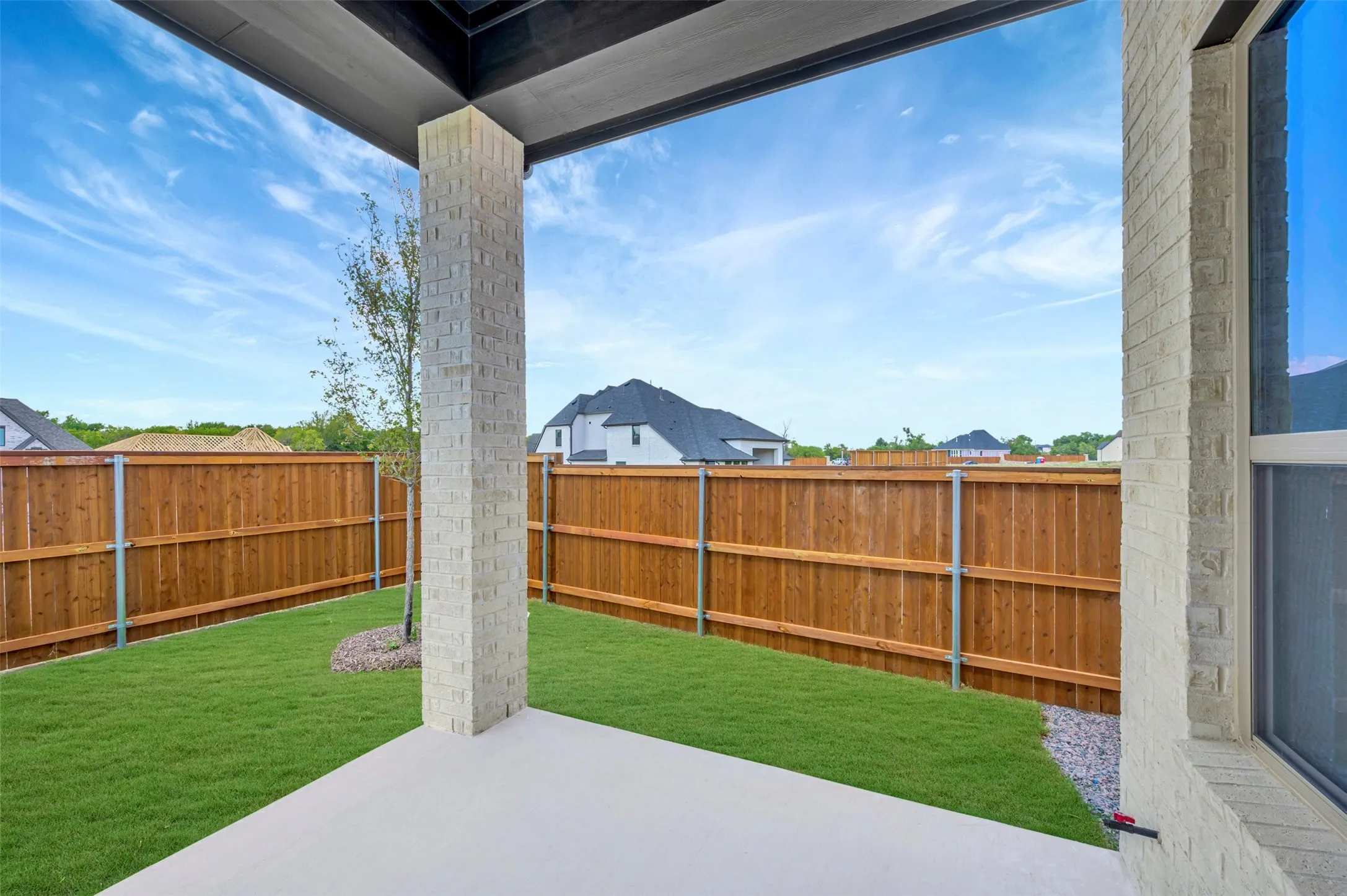 Covered patio featuring concrete flooring, a brick column, and a wood privacy fence