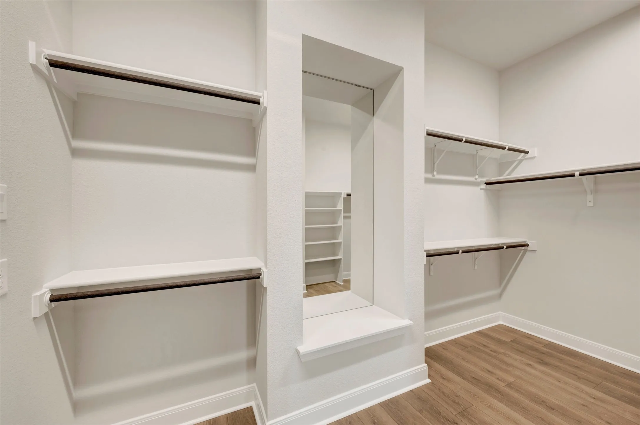 Walk-in closet with multiple shelving units, integrated hanging rods, a full-length mirror, and wood-finish flooring