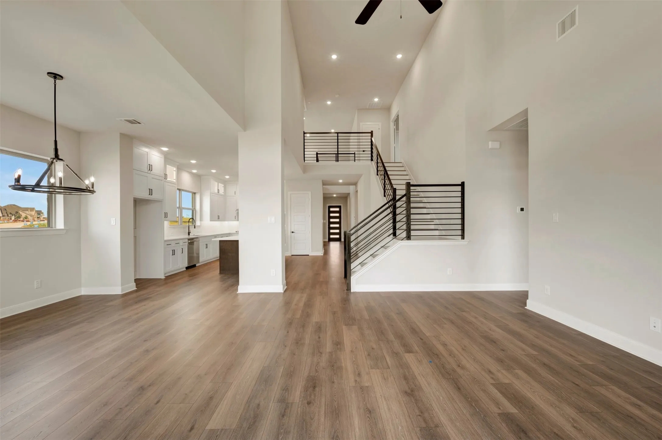Vaulted ceilings, wood-finish flooring, two-story staircase with horizontal bar railing, recessed lighting, and a chandelier fixture