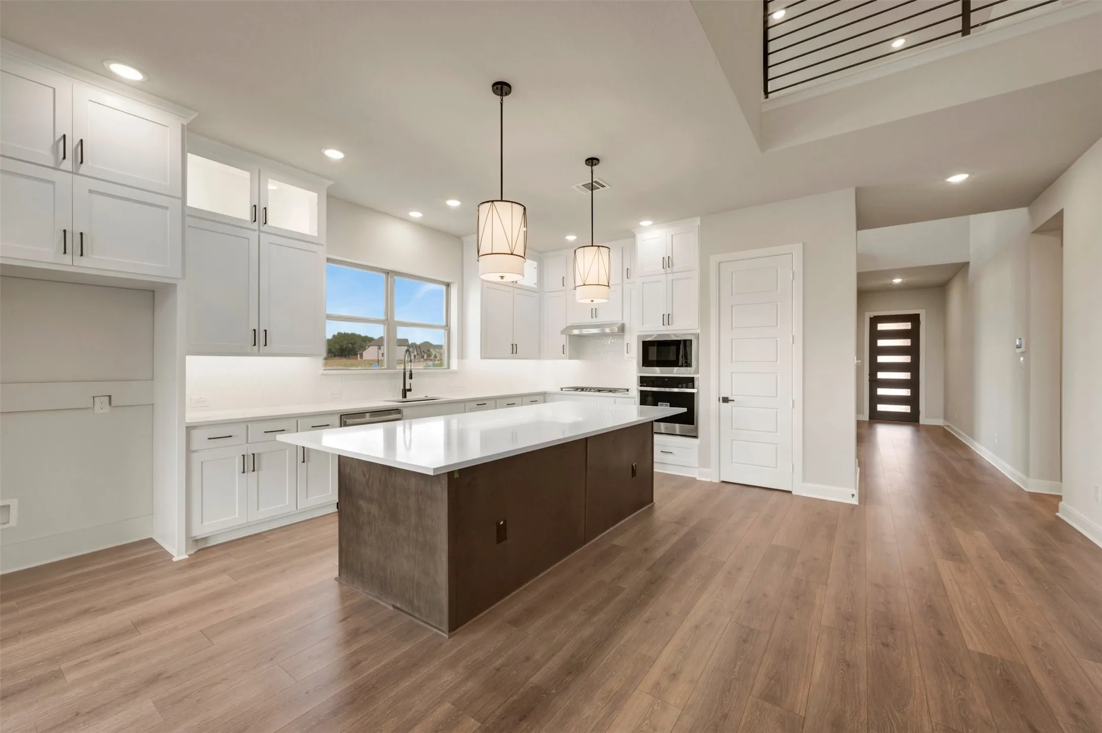 Spacious kitchen featuring an expansive island, stainless steel appliances, white cabinetry, and wood-finish flooring