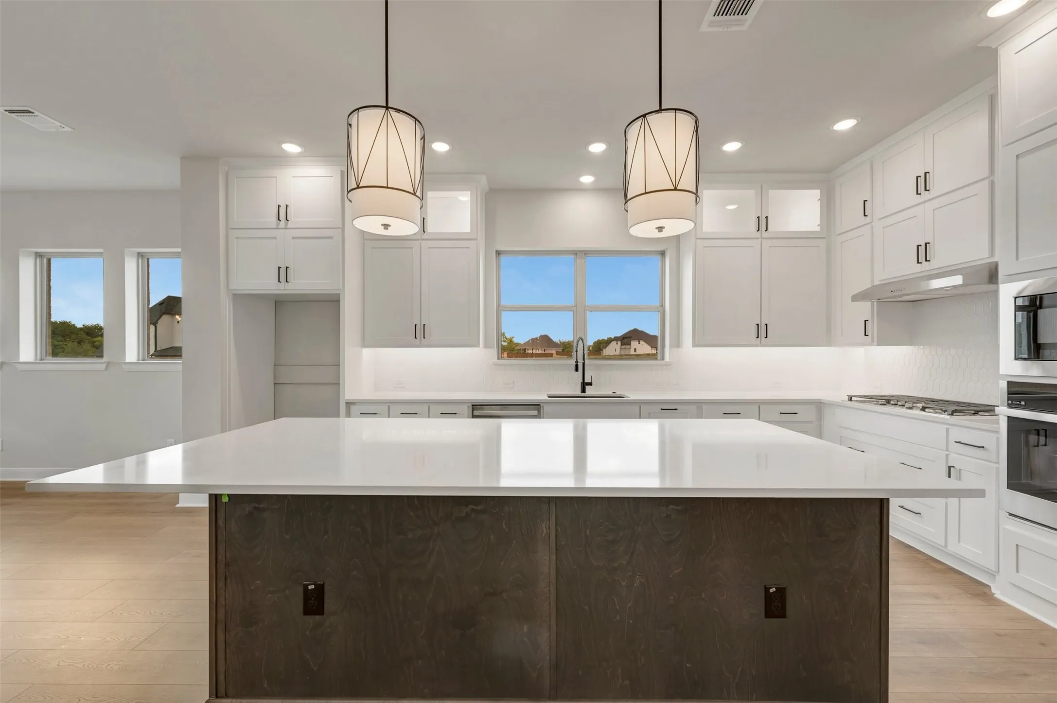 Kitchen featuring a large island with a light-toned countertop, white cabinetry with dark hardware, a stainless steel range hood, and wood-finish flooring