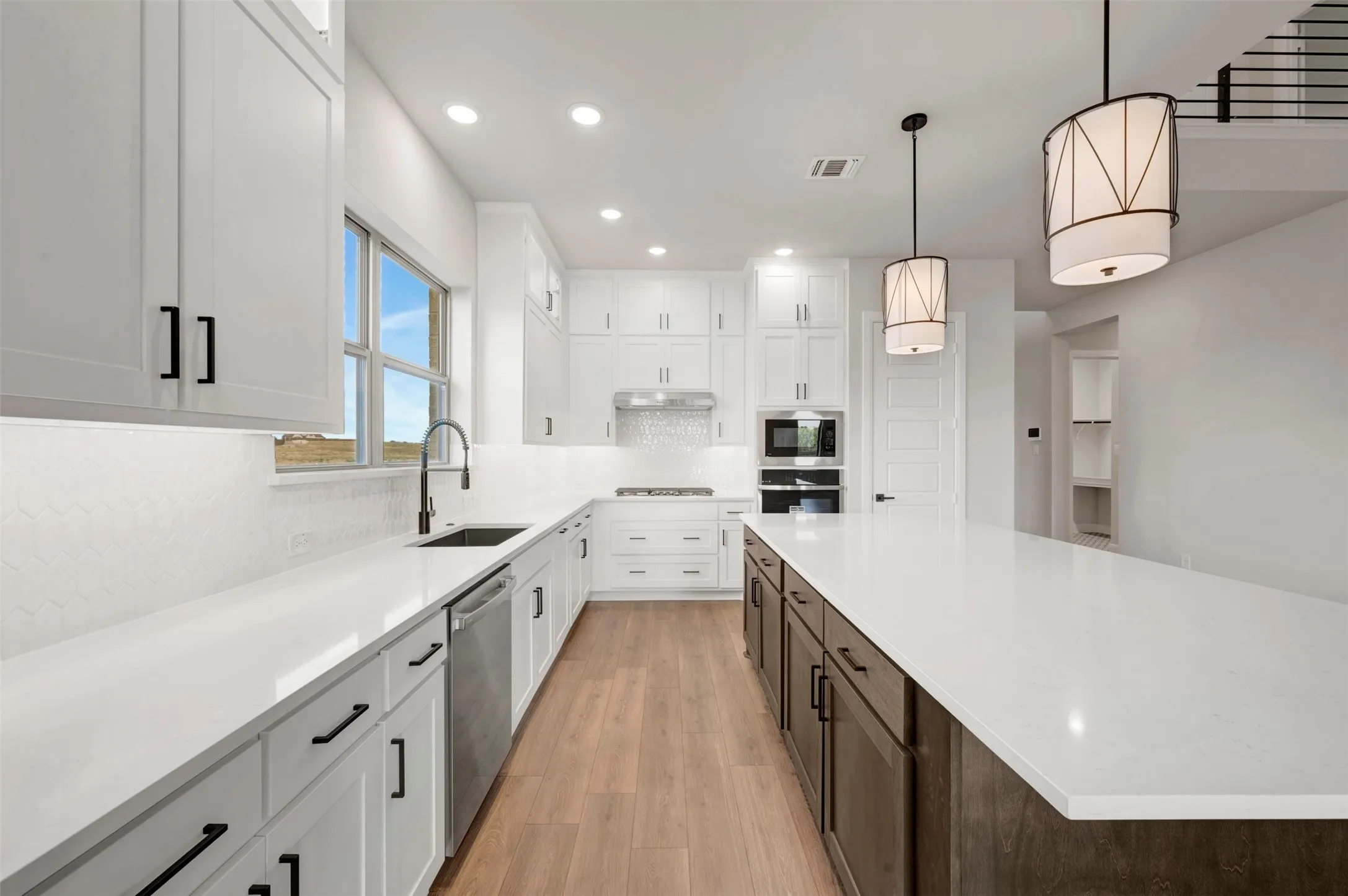 White shaker cabinetry, stainless steel appliances, central island with seating, wood-finish flooring, and recessed lighting