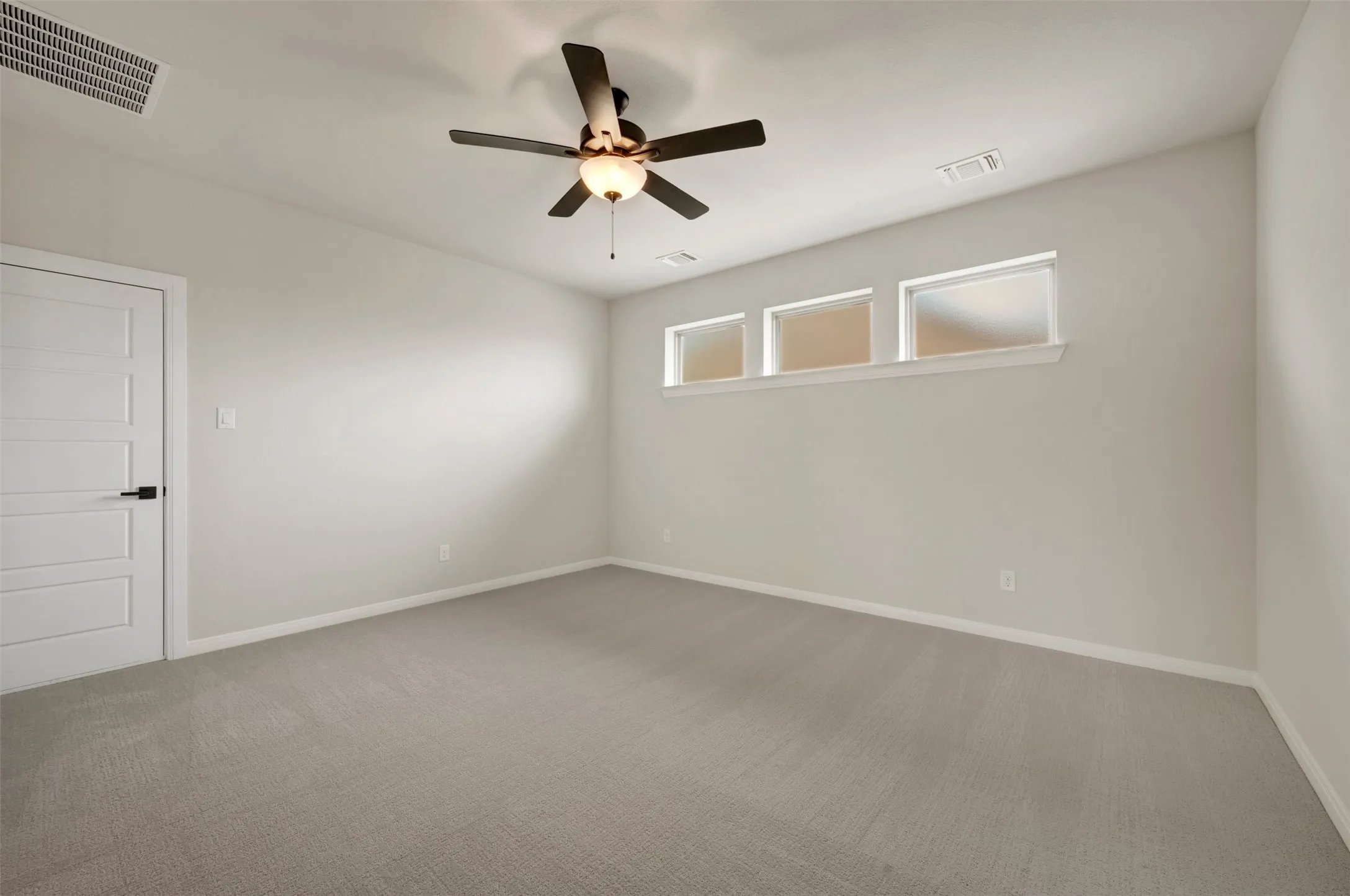 Recessed windows providing natural light, ceiling fan with integrated lighting, paneled door with matte black hardware, and neutral-toned carpeting
