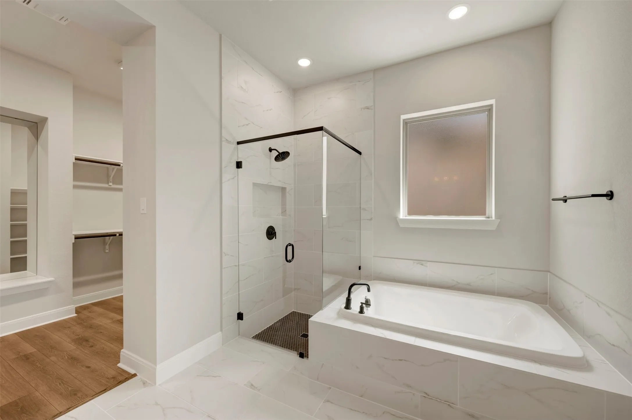 Spacious bathroom featuring a built-in soaking tub, a glass-enclosed shower with black fixtures, and marble-look tile flooring