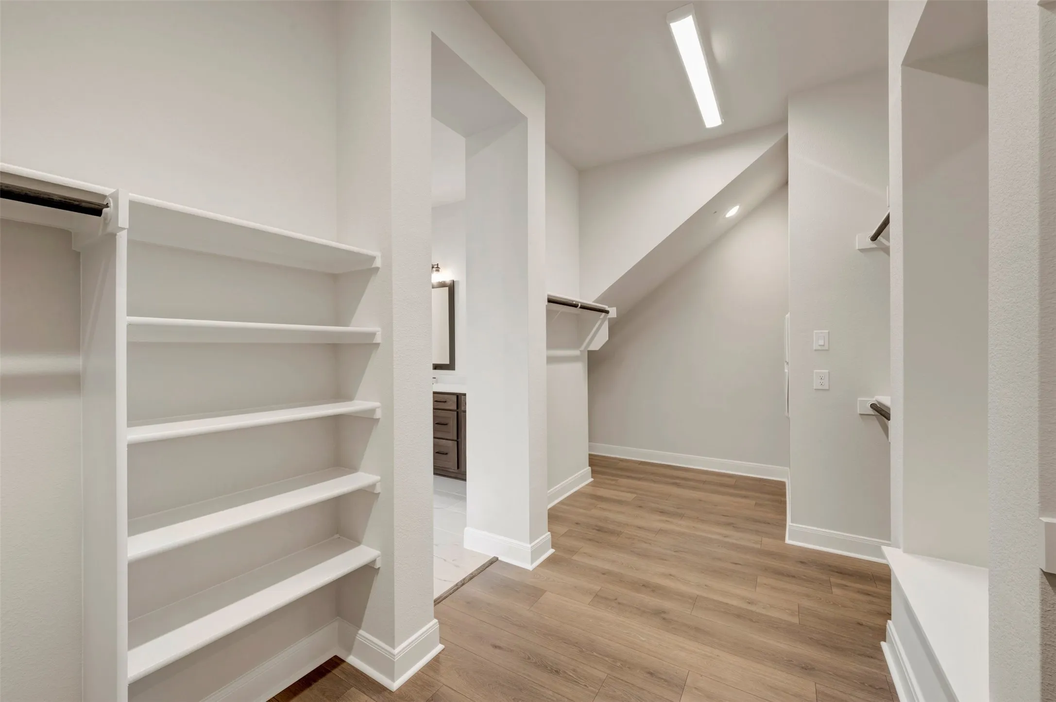 Walk-in closet featuring wood-finish flooring, built-in shelving, multiple hanging rods, and recessed lighting