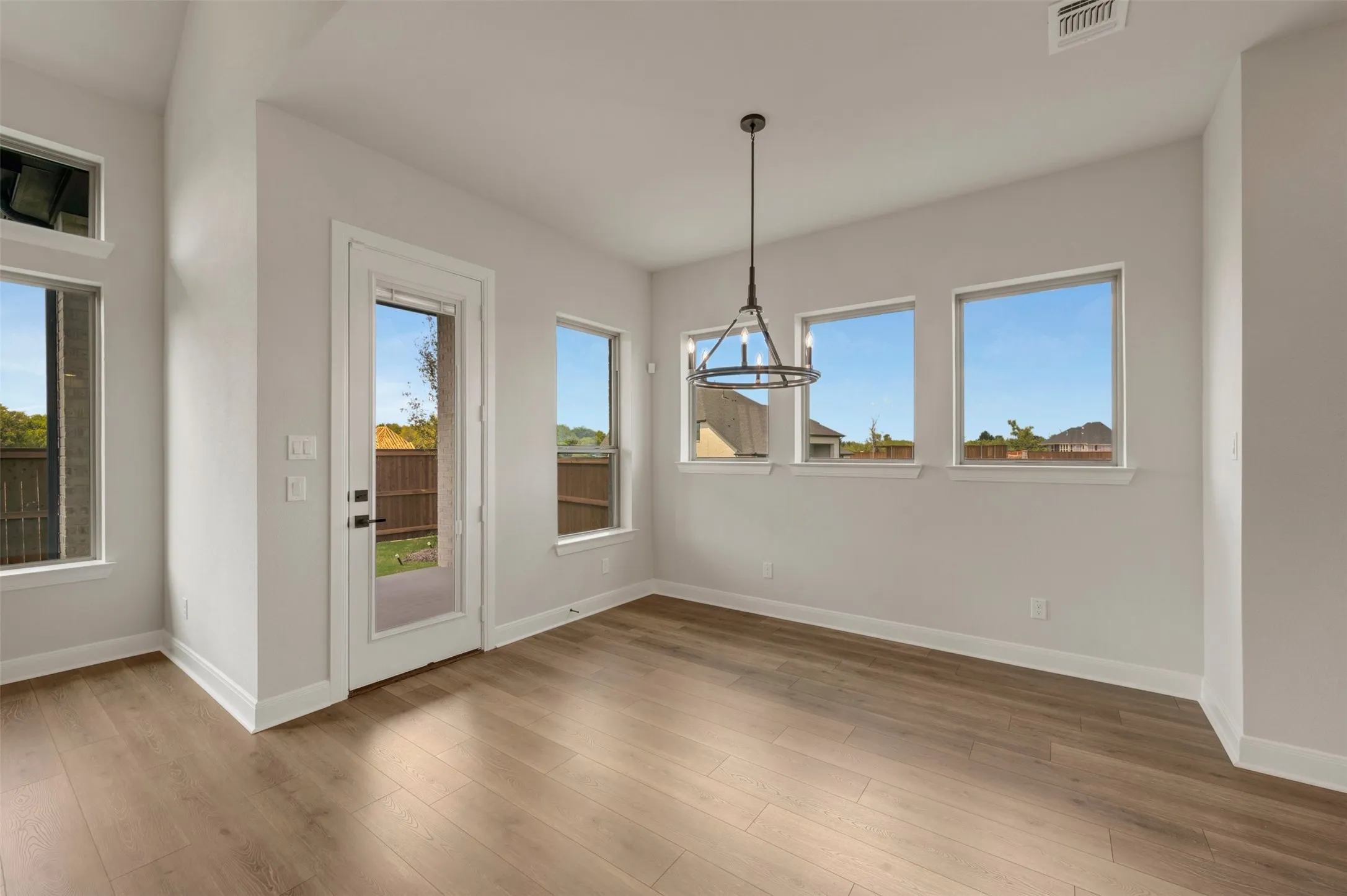 Wood-finish flooring, multiple windows, a full-lite exterior door, a contemporary chandelier, and a neutral color palette