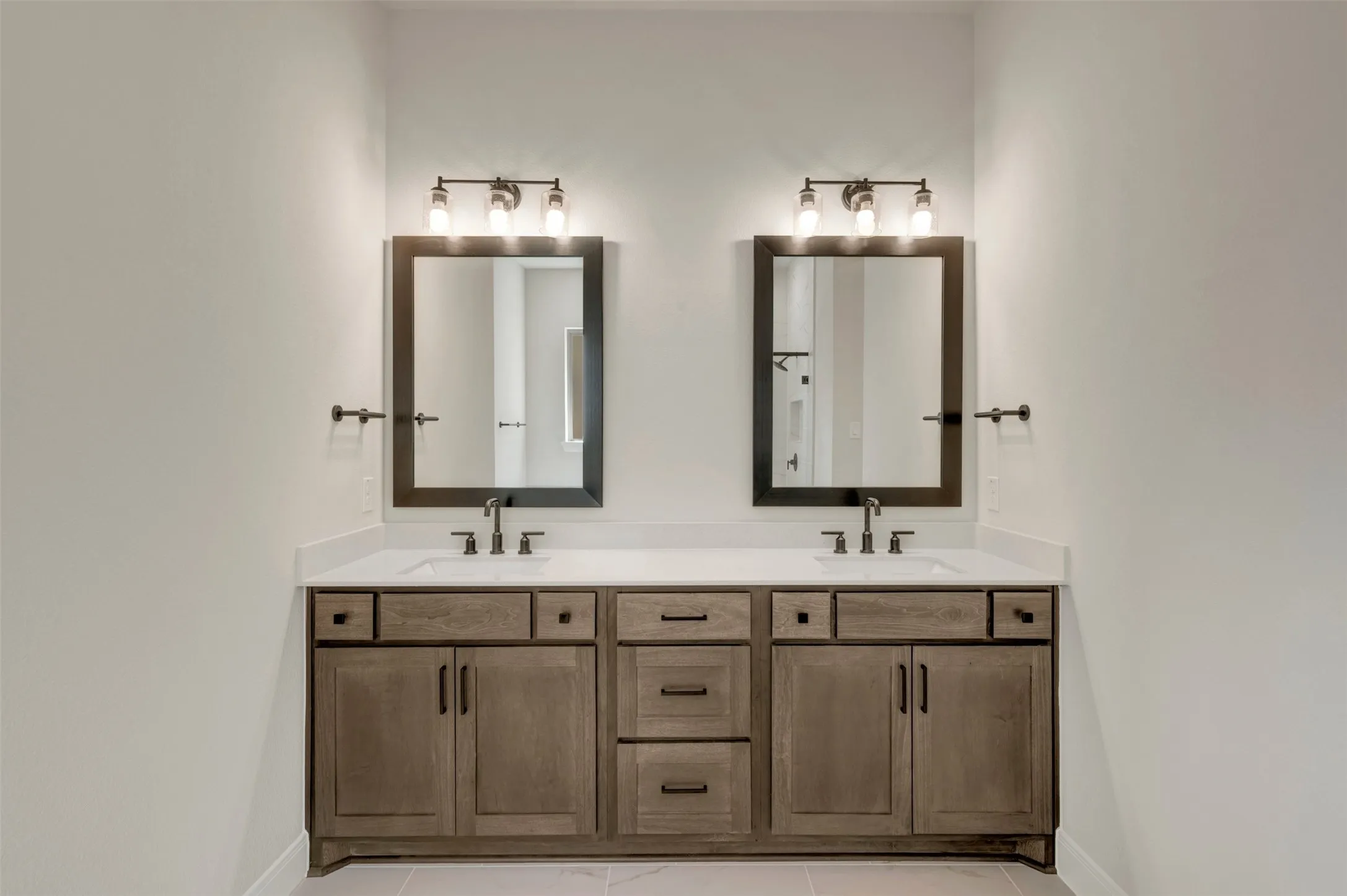 Dual vanity featuring a light-toned countertop, wood-finish cabinetry, and framed mirrors with overhead lighting