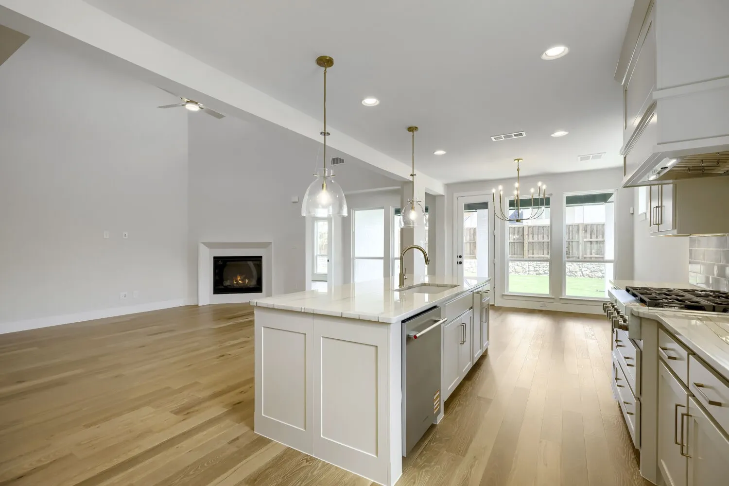 Open-concept living area featuring a kitchen island with sink, stainless steel appliances, wood-finish flooring, a contemporary fireplace, and high vaulted ceilings