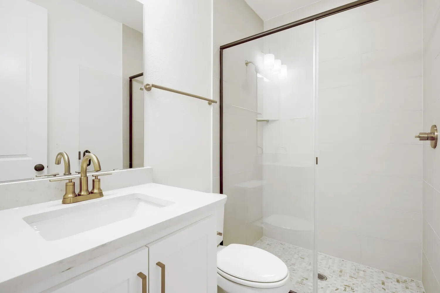 Bathroom featuring a white vanity with a light-toned countertop, a shower enclosure with clear glass and dark-framed doors, white subway-style shower wall tiles, and mosaic-patterned shower floor tiles