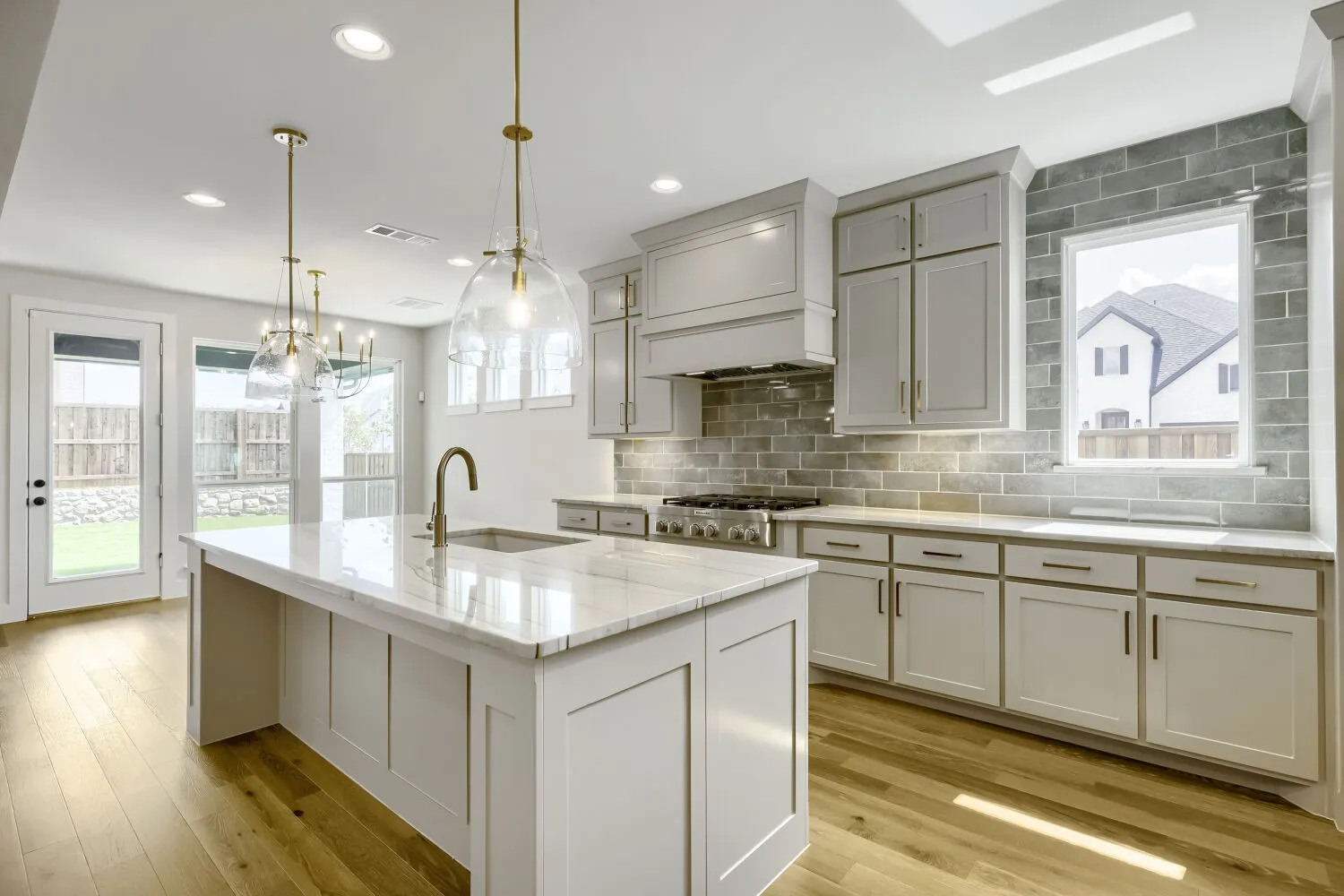 Kitchen featuring a central island with a sink and gold-finish faucet, light wood-finish flooring, recessed lighting, white cabinetry, a tiled backsplash, and stainless steel appliances