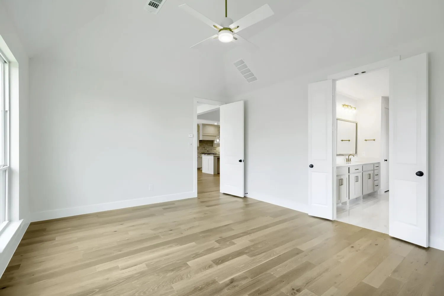 Spacious interior room featuring wood-finish flooring, white walls, and a vaulted ceiling with a white ceiling fan