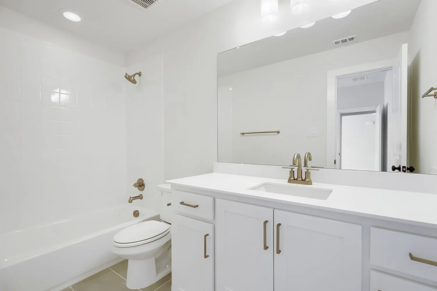 White vanity with ample storage, integrated sink, and brushed brass fixtures, complemented by a full-width mirror and overhead lighting