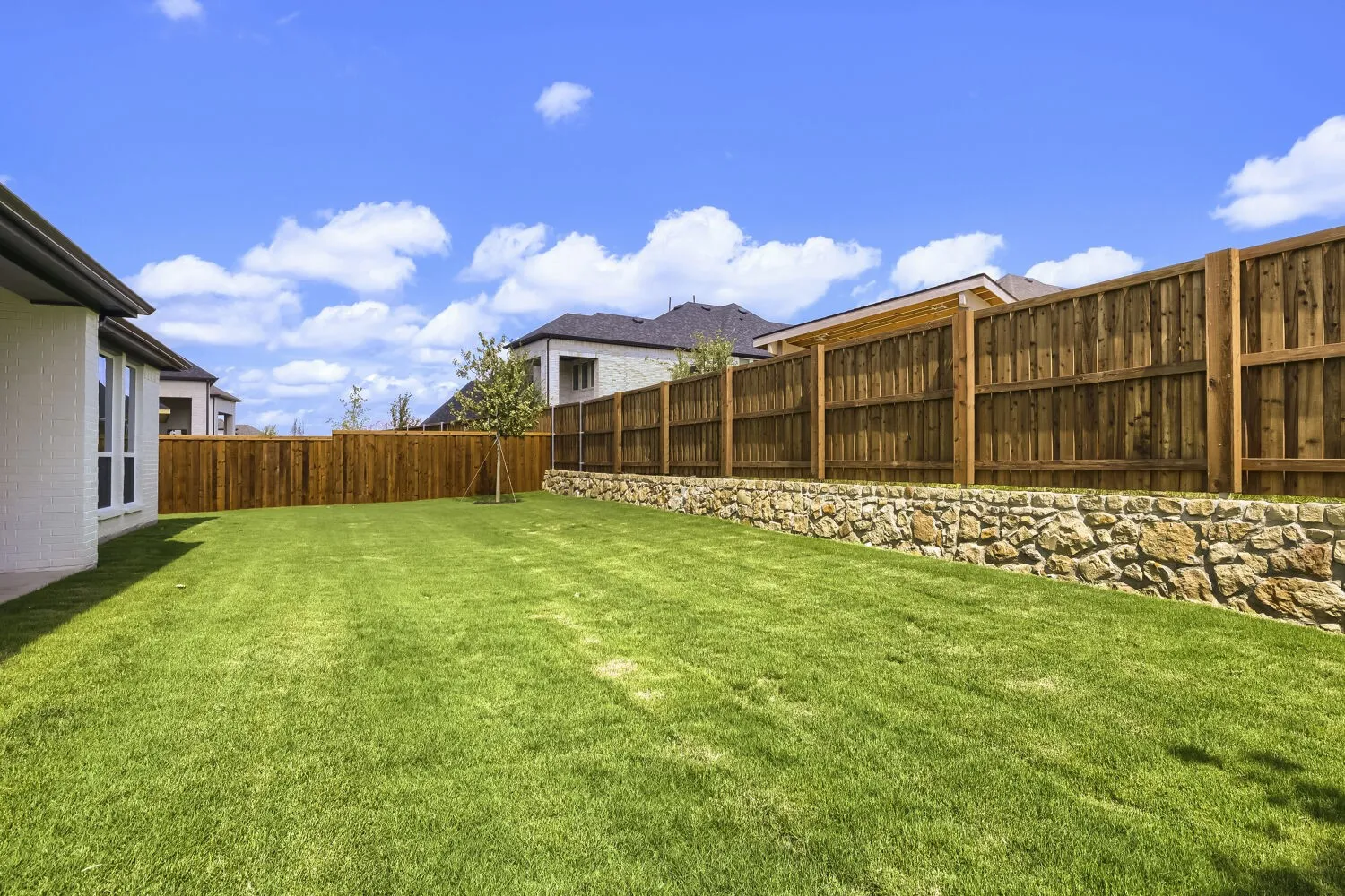 Expansive green lawn with a newly installed wood privacy fence and a stone retaining wall