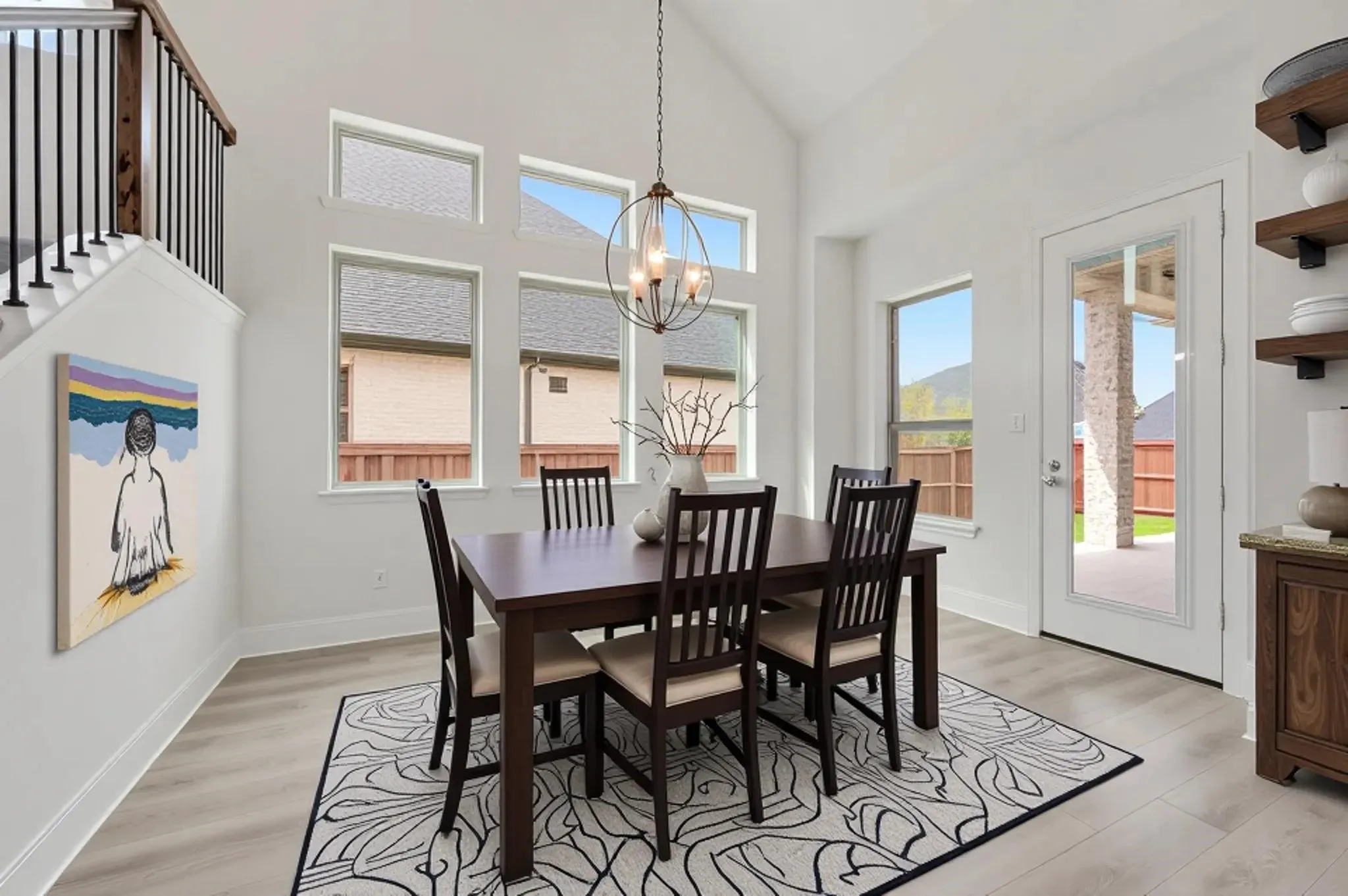 Vaulted ceiling with an orb chandelier, light wood-finish flooring, and multiple windows