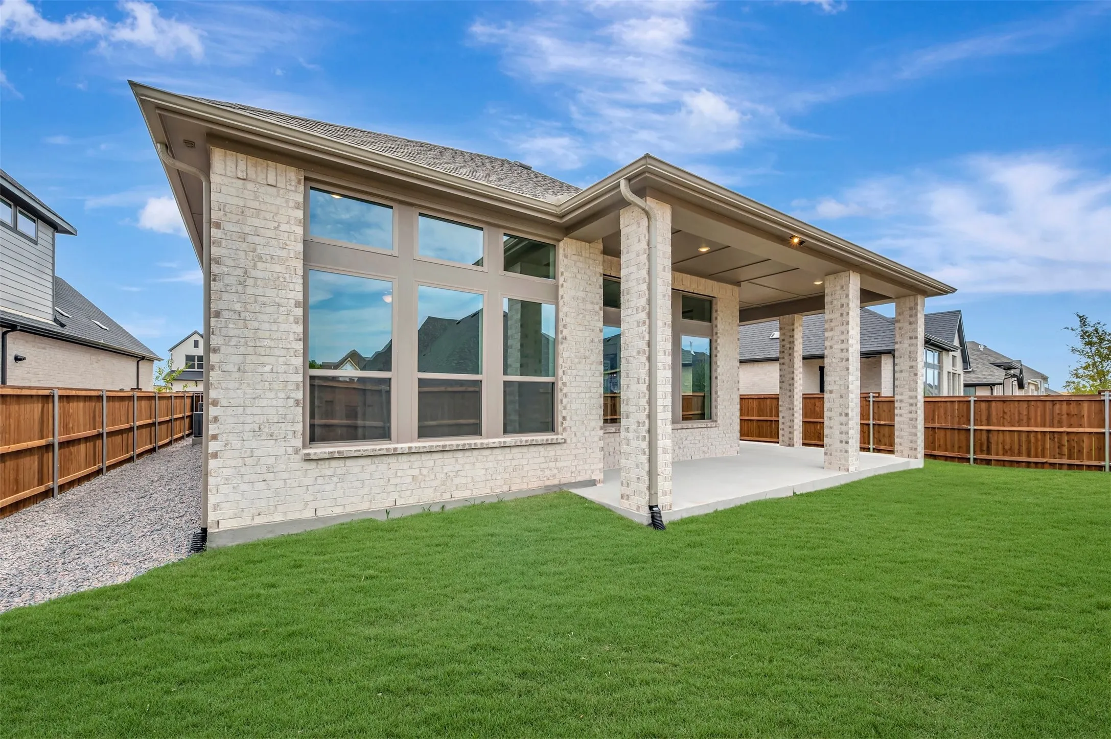Expansive backyard featuring a manicured lawn, a covered patio with recessed lighting, and a full brick exterior