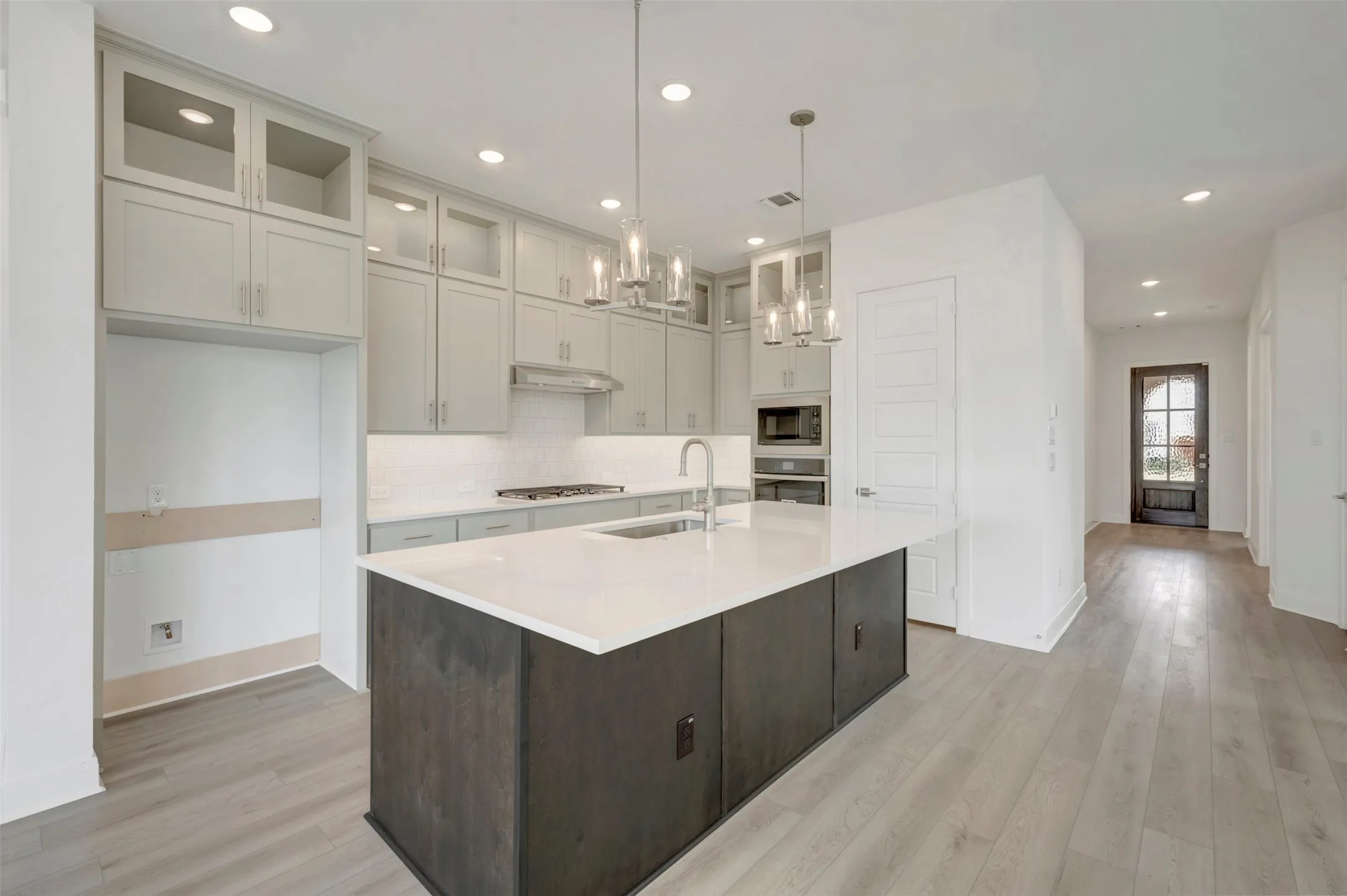 Modern kitchen featuring a large central island with a sink, light gray cabinetry, and recessed lighting