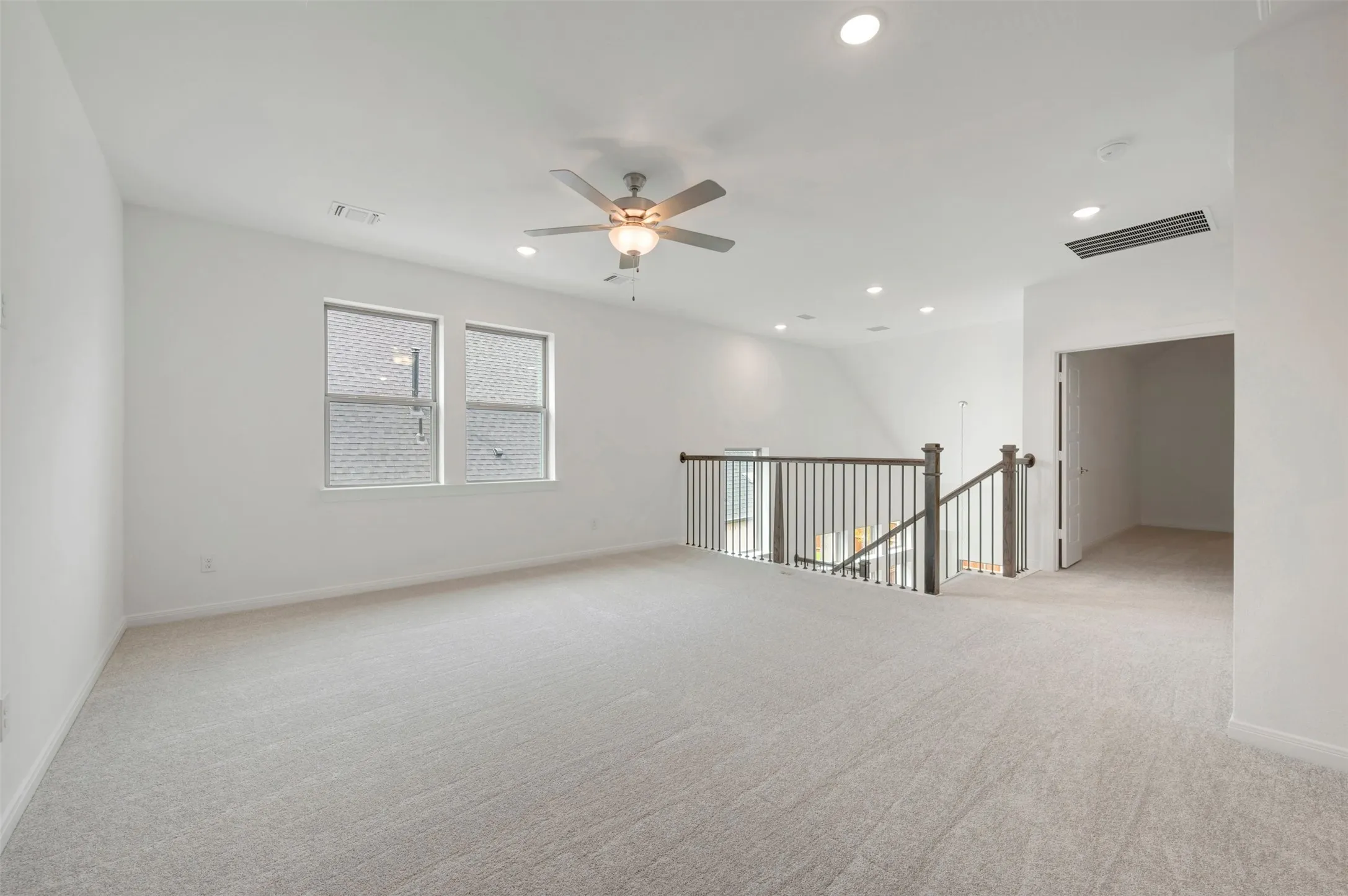 Expansive carpeted loft space featuring recessed lighting, a ceiling fan, and a wood and metal baluster railing