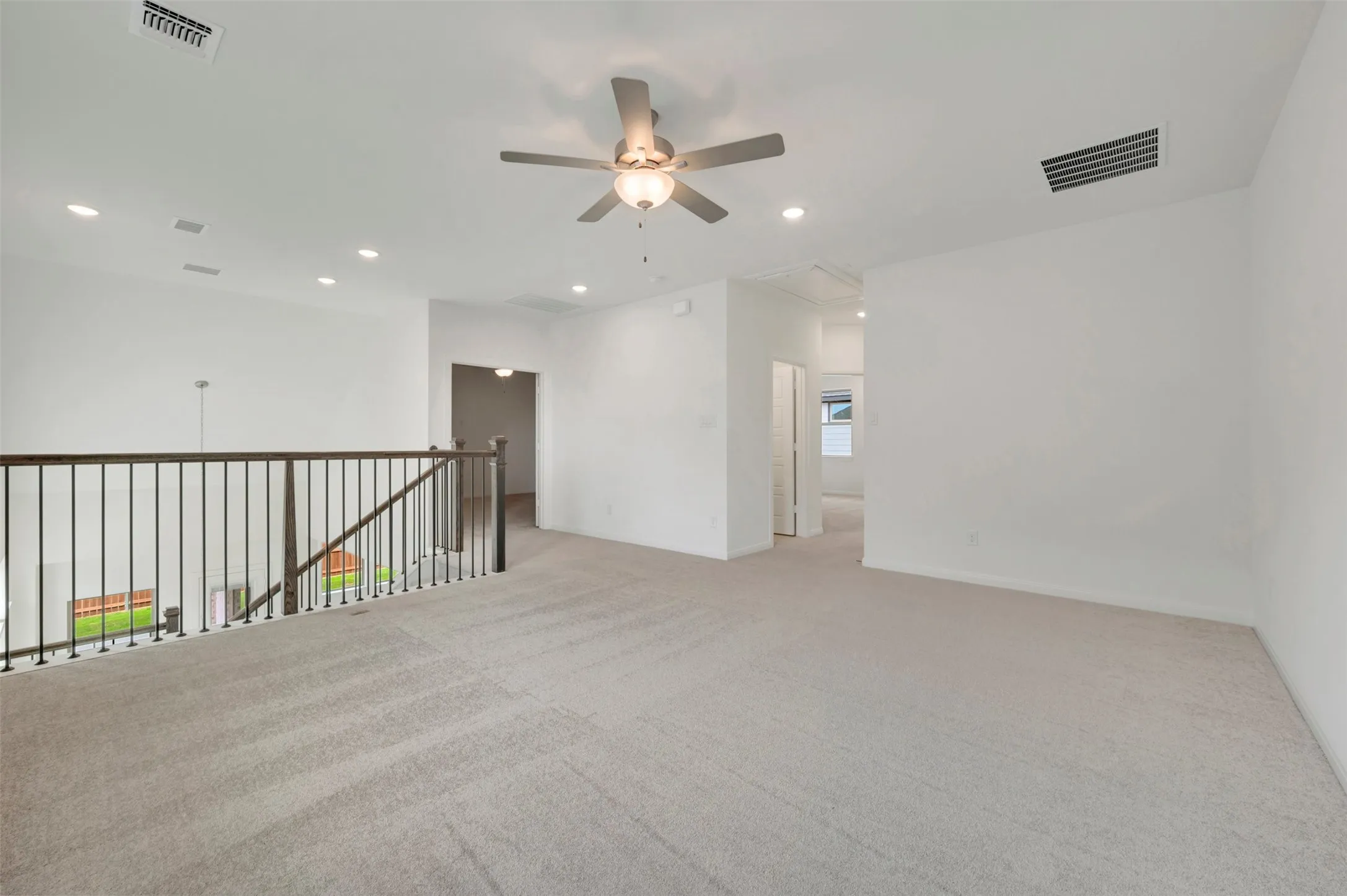 Expansive carpeted loft with recessed lighting, a ceiling fan, and a wood railing with black metal spindles