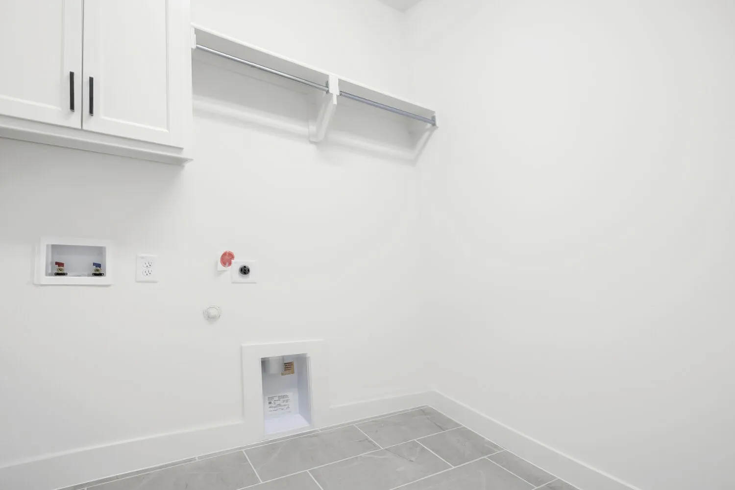 Dedicated laundry space featuring white cabinetry with black hardware, an integrated hanging rod, and light gray tile flooring
