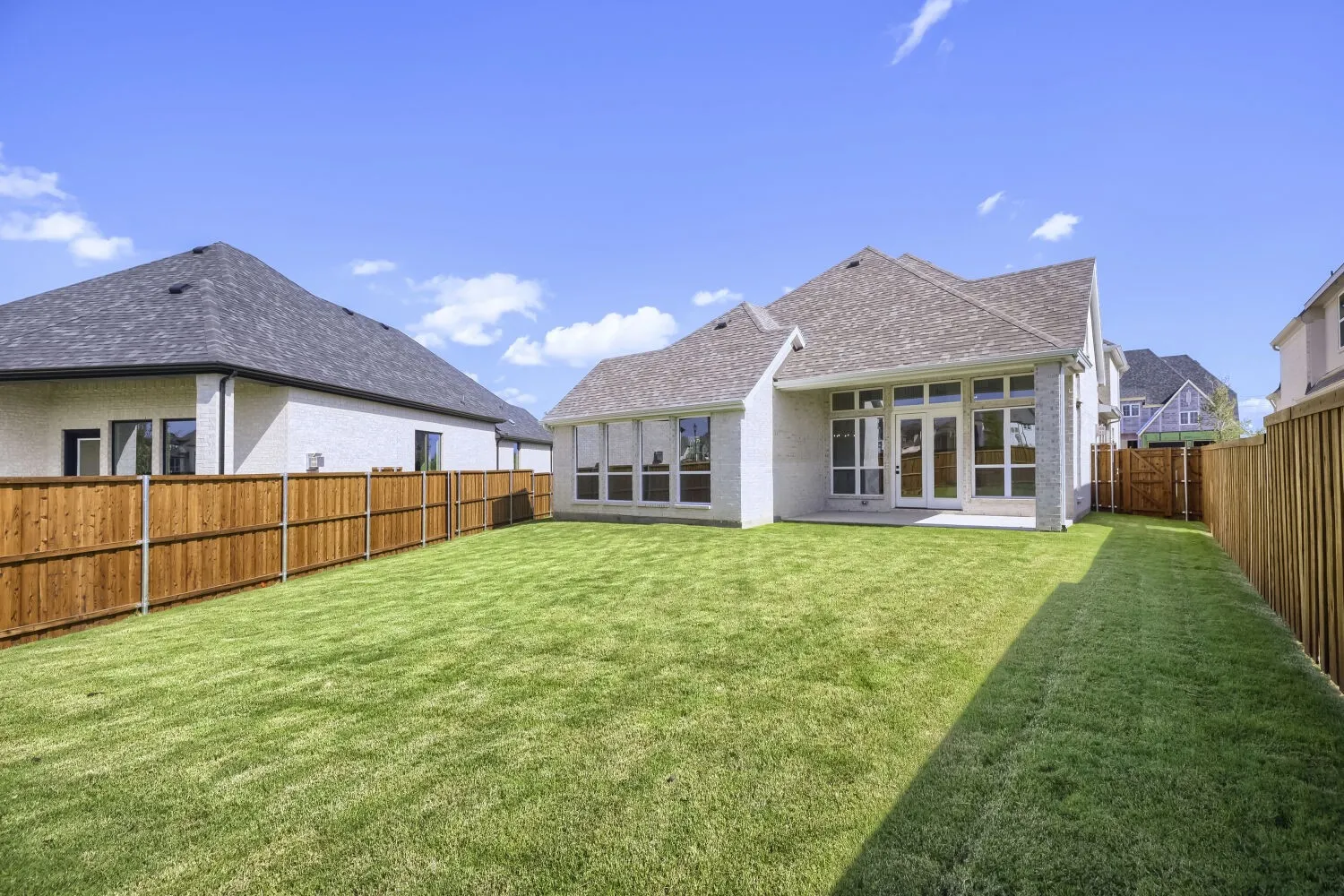 Spacious backyard featuring a lush green lawn, full wood privacy fencing, and an expansive concrete patio