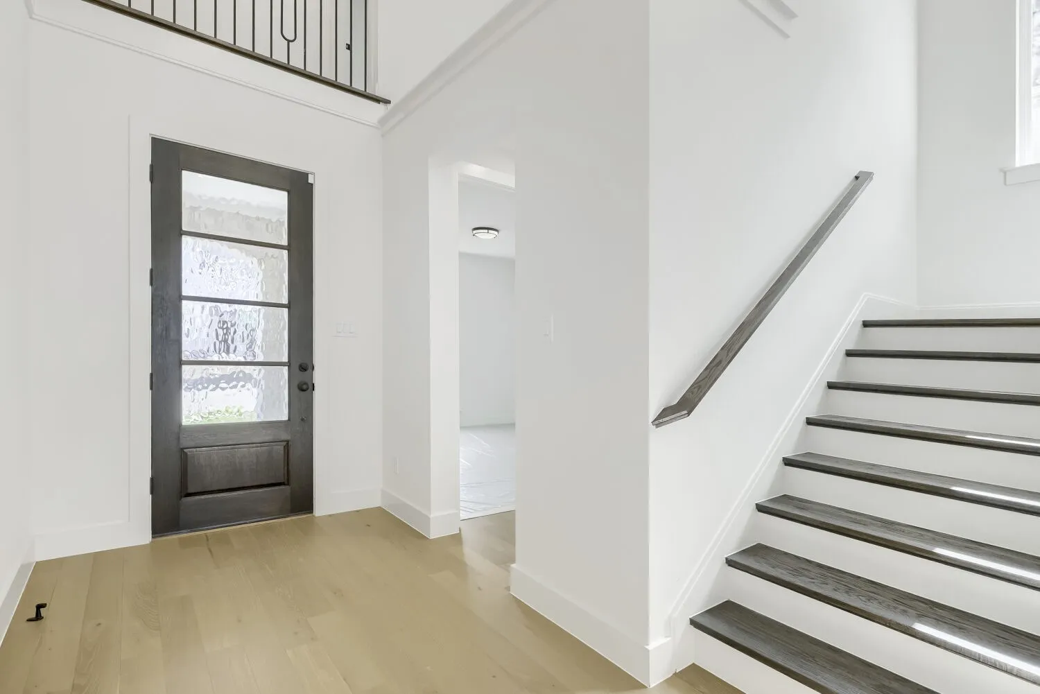 Entryway featuring a dark wood-finish door with frosted glass panels, light wood-finish flooring, a contemporary staircase with dark wood-finish treads and a sleek handrail, crisp white walls, and crown molding