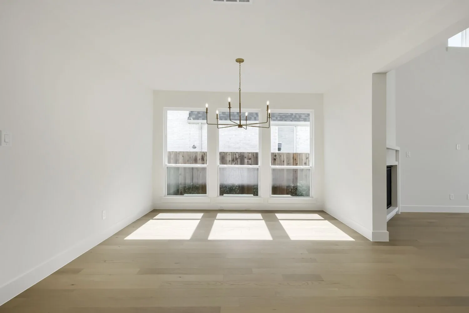 Spacious interior room featuring light wood-finish flooring, white walls, and a contemporary chandelier