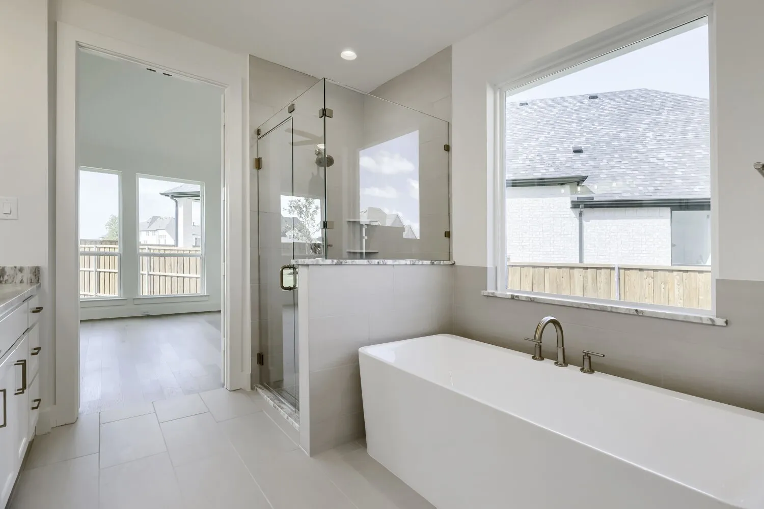 Freestanding soaking tub with a brushed nickel faucet, large window, and tile surround