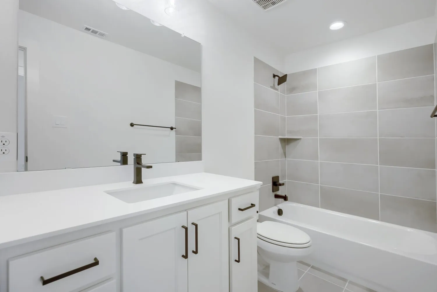 Bathroom featuring a white vanity with an integrated sink, dark bronze fixtures, a full-width mirror, a tiled shower/tub combination, and recessed lighting