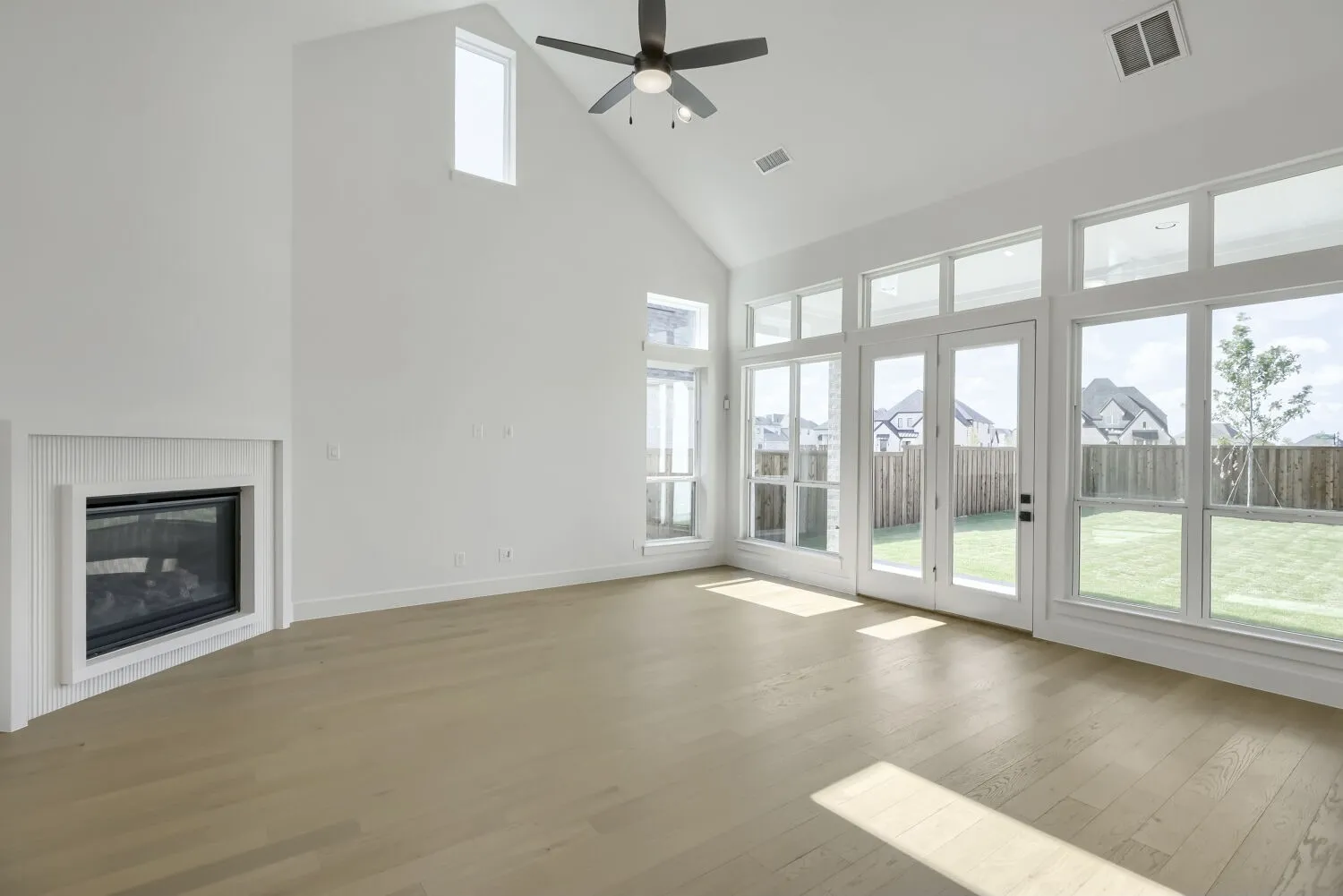 Spacious room featuring vaulted ceilings, wood-finish flooring, and a contemporary fireplace with a decorative mantel