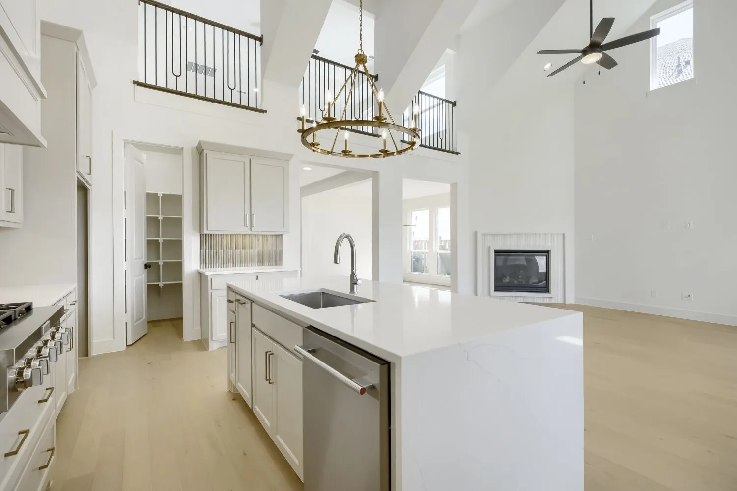 Open concept kitchen featuring a large central island with an undermount sink and integrated dishwasher, light wood-finish flooring, white cabinetry, and light-toned countertops