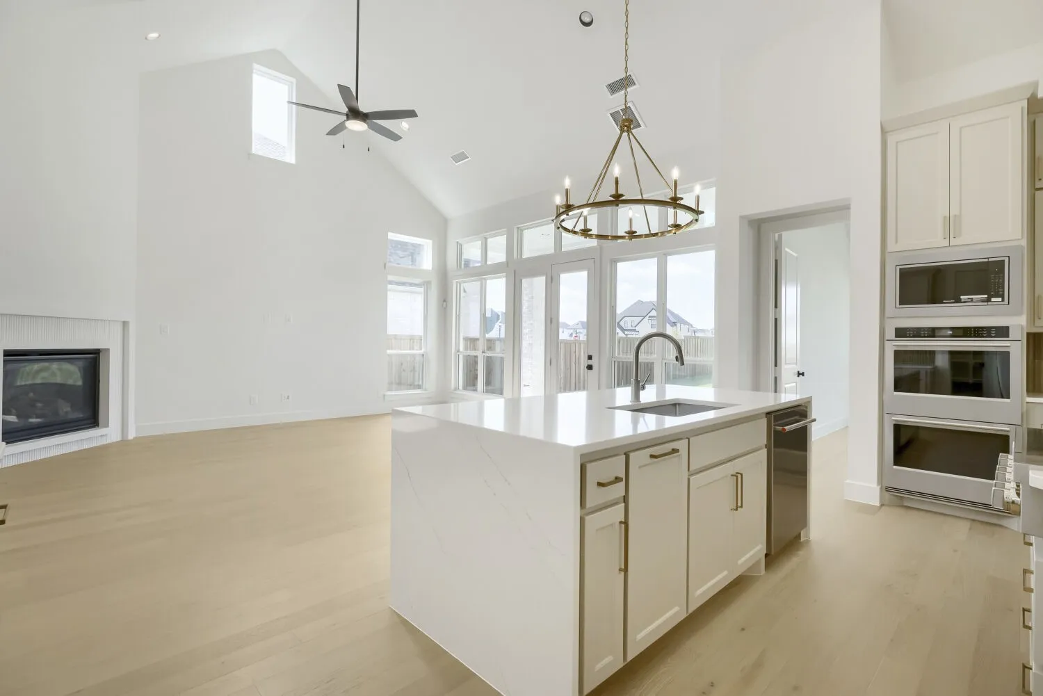 Open-concept kitchen and living area featuring high vaulted ceilings, light wood-finish flooring, a contemporary fireplace, a kitchen island with a sink, and integrated stainless steel appliances