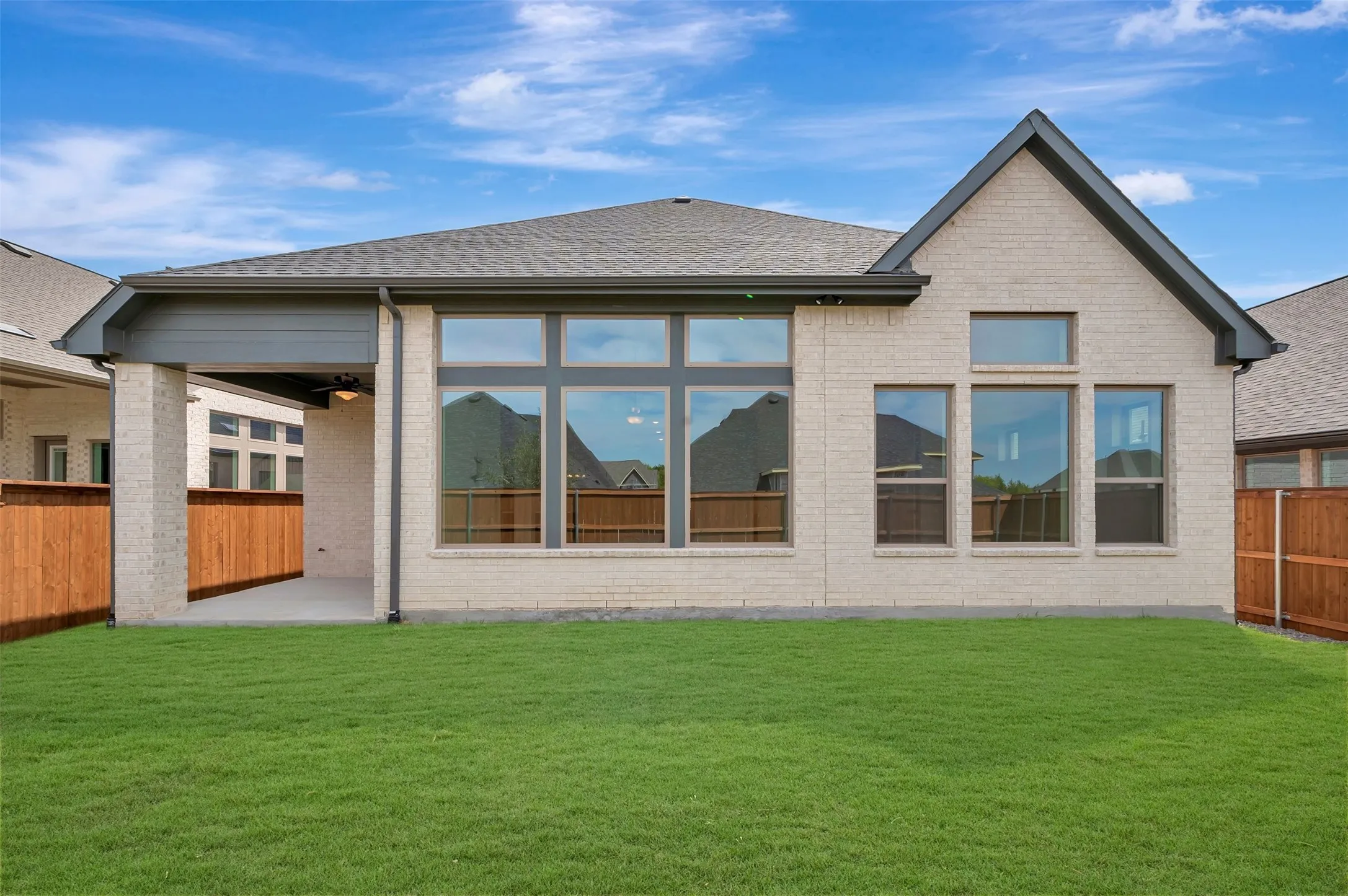 Expansive backyard with a manicured lawn, covered patio, light brick exterior, and multiple large windows