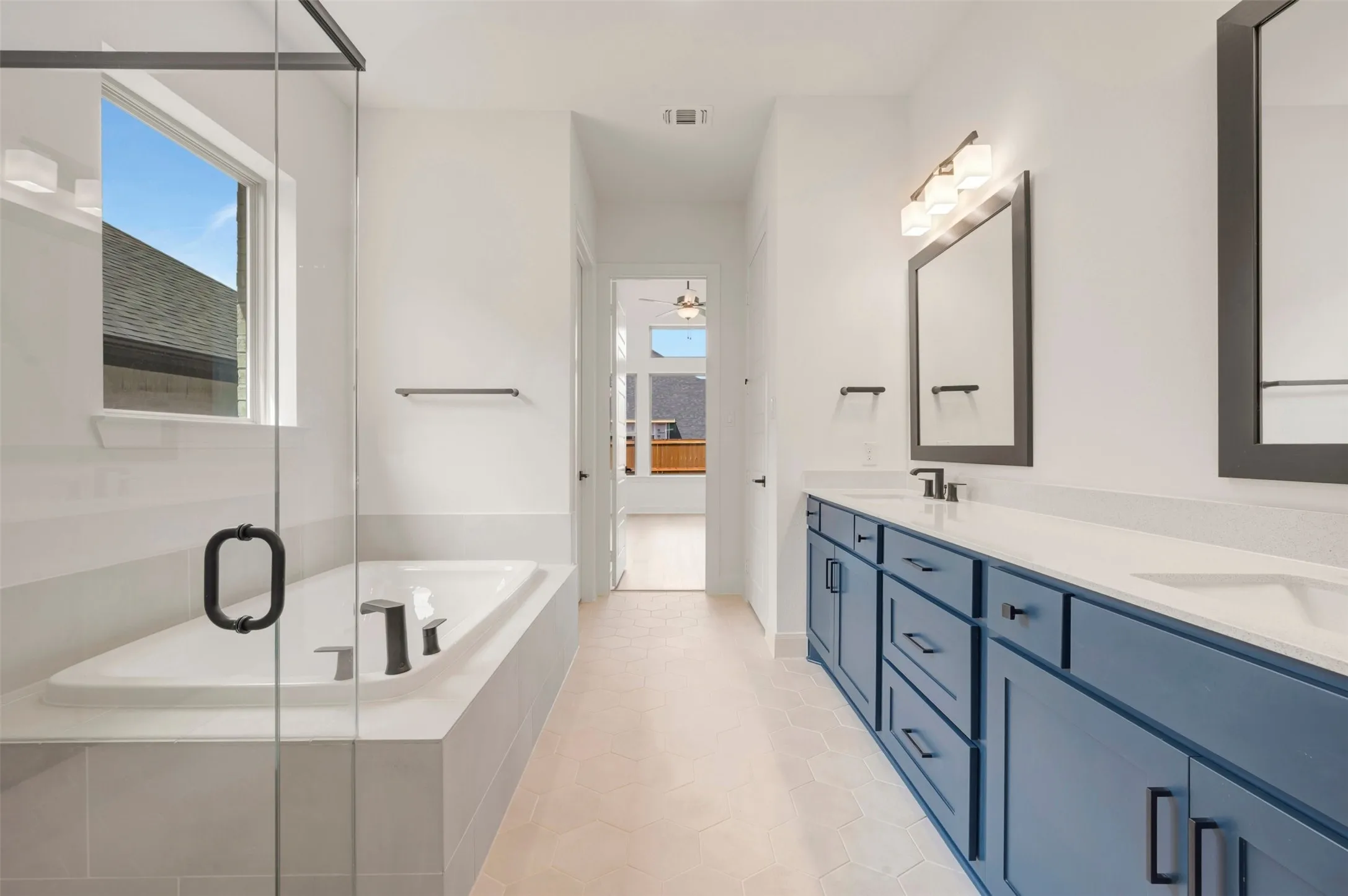 Bathroom featuring a built-in soaking tub, glass-enclosed shower, dual vanity with blue cabinetry, and hexagonal floor tiling