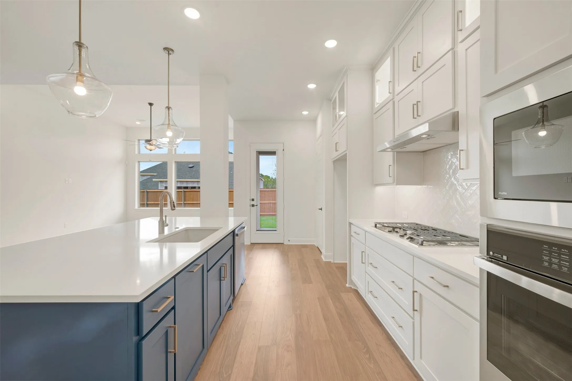 Well-appointed kitchen featuring a large island with sink, white shaker cabinetry, stainless steel appliances, and wood-finish flooring