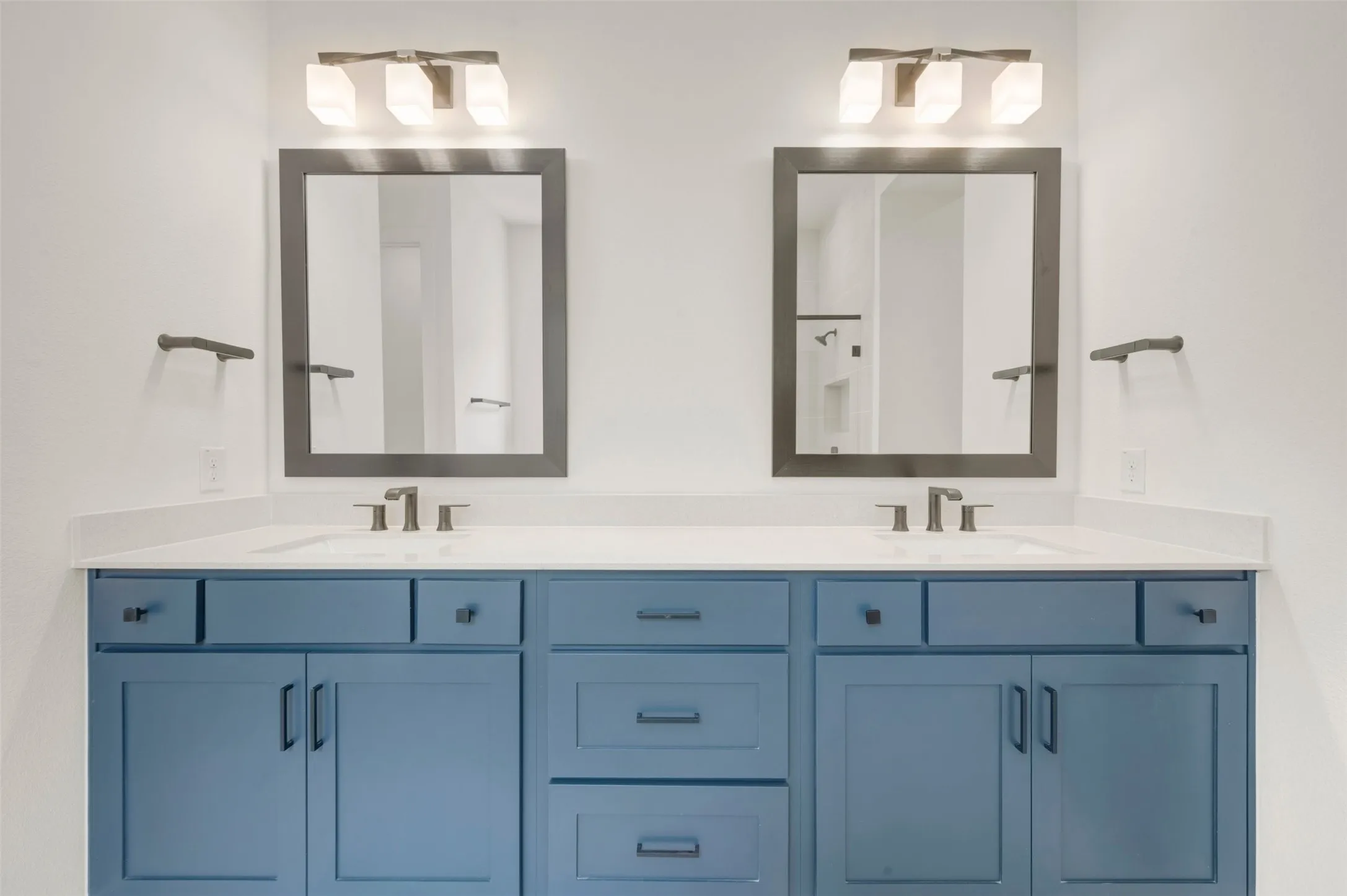Dual vanity with blue cabinetry, white countertops, rectangular undermount sinks, and dark framed mirrors