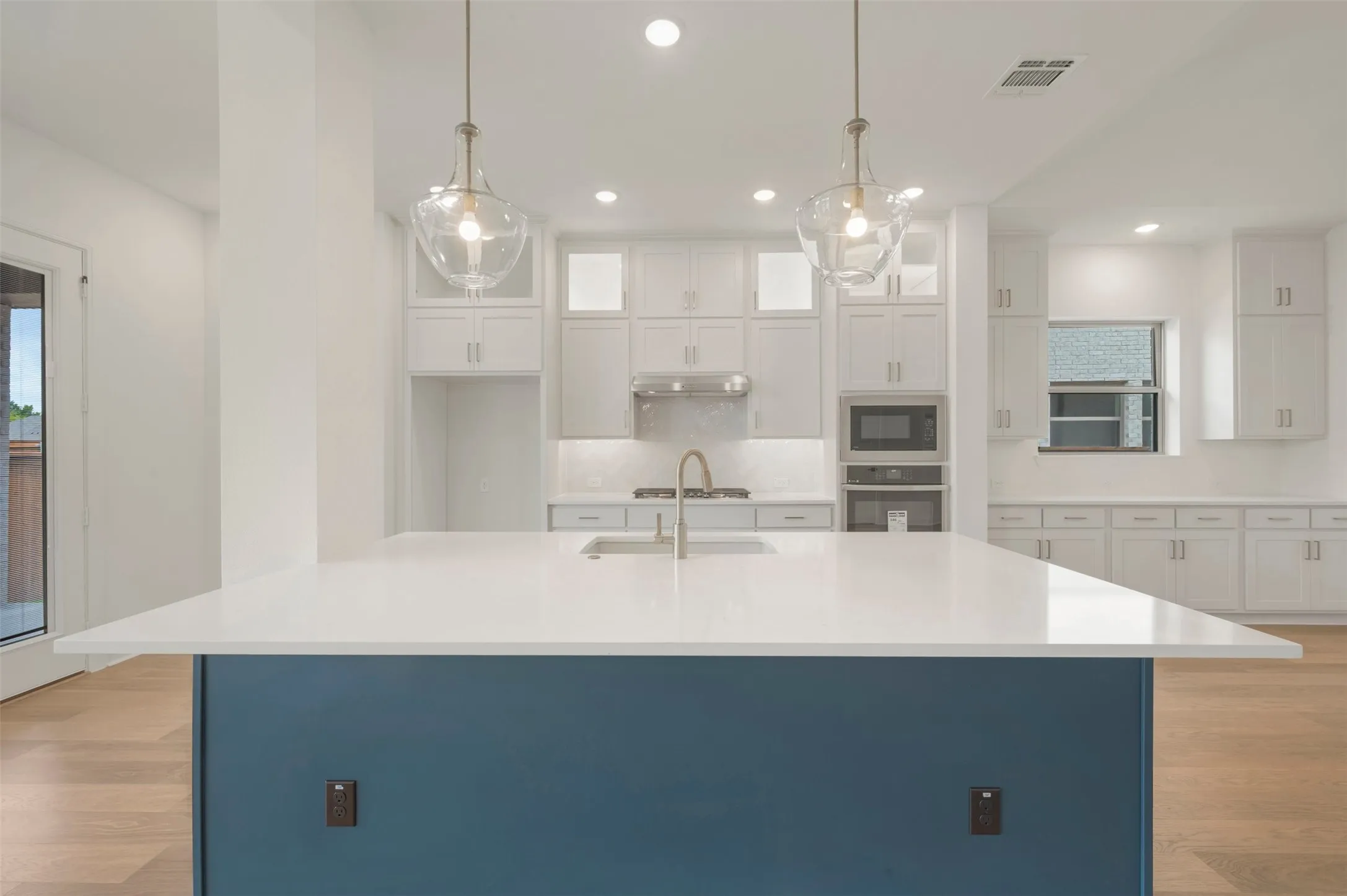 Kitchen with a large island featuring a white countertop, white cabinetry, integrated appliances, and wood-finish flooring