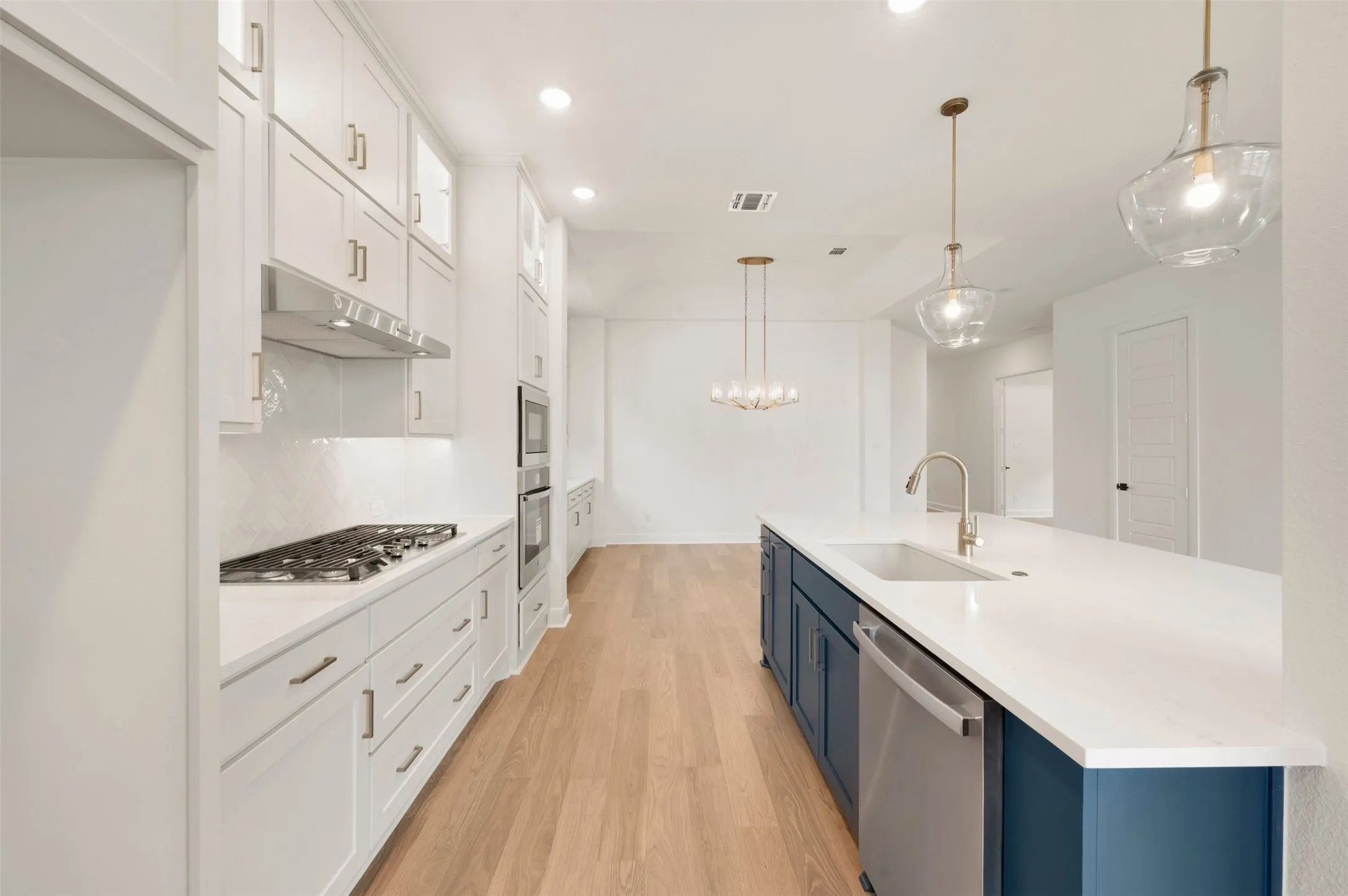 Gourmet kitchen with white cabinetry, gas cooktop, built-in double ovens, and a large island featuring a single-basin sink and integrated dishwasher
